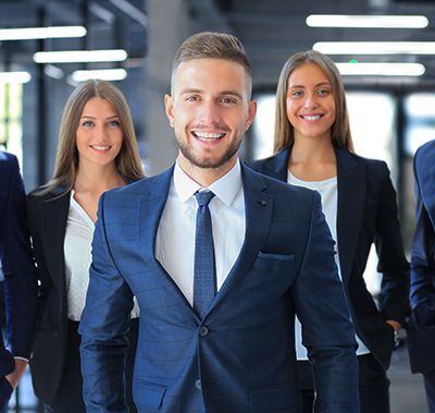 Smiling business team in a modern office. Man in blue suit at front, women in black suits behind.