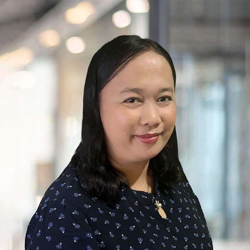 Woman with black hair in navy top, smiling in an office setting.