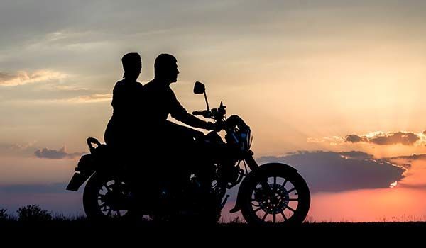 Silhouette of two people riding a motorcycle at sunset.
