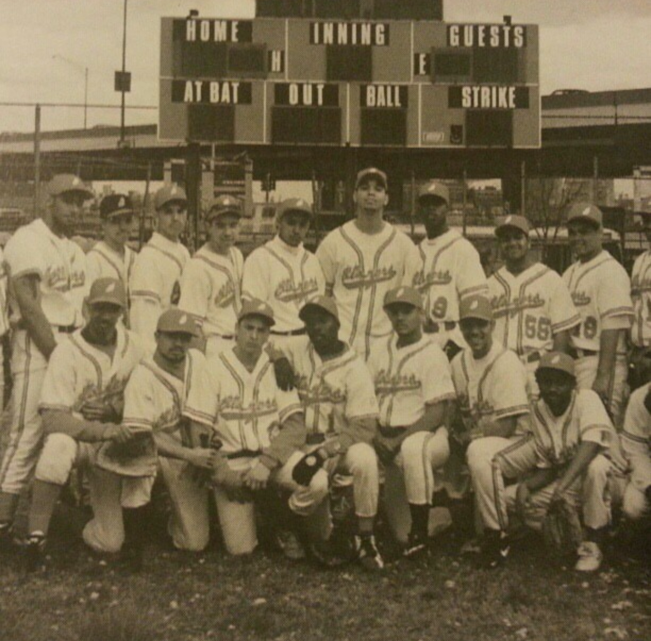 A group of baseball players pose in front of a scoreboard that says guests