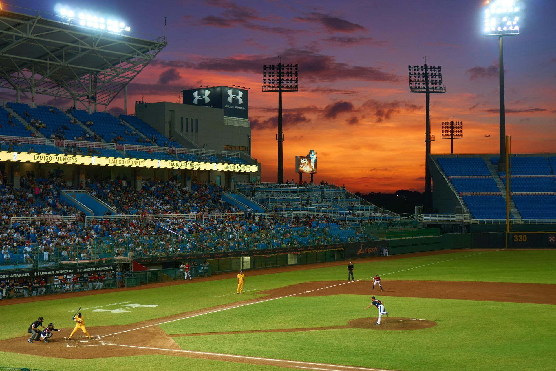 A baseball game is being played in a stadium at sunset