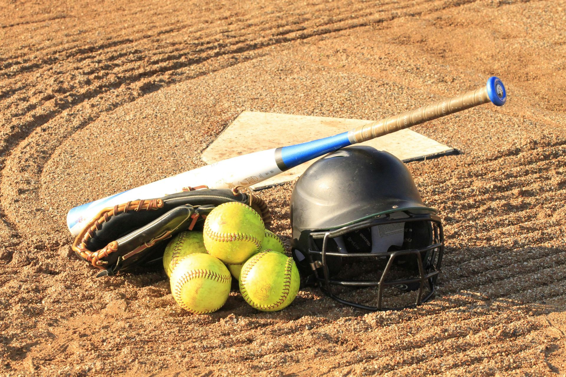A baseball bat , helmet , glove and balls on a dirt field