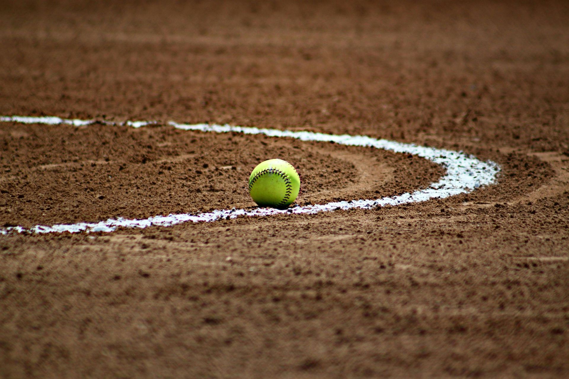 A tennis ball is sitting on the line of a tennis court.