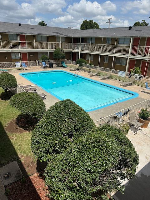 Apartment complex courtyard with a pool, bushes, and second-floor balconies. Blue pool and sky.