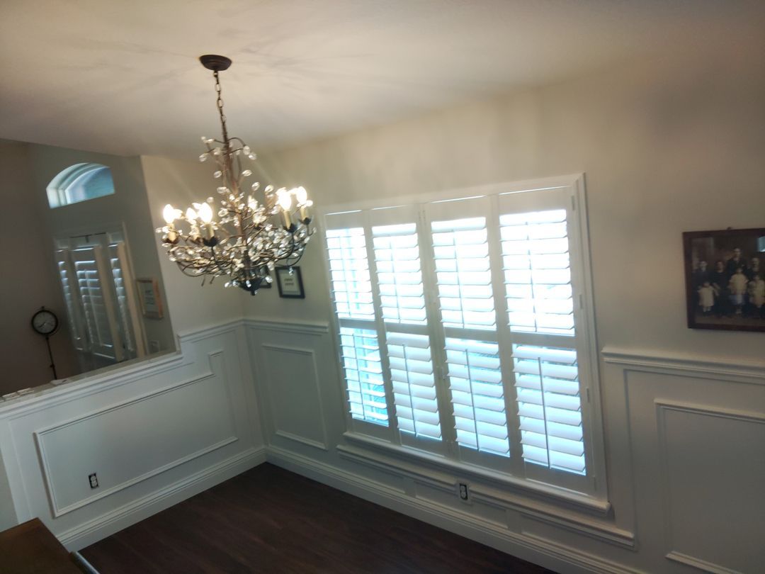A dining room with white shutters and a chandelier