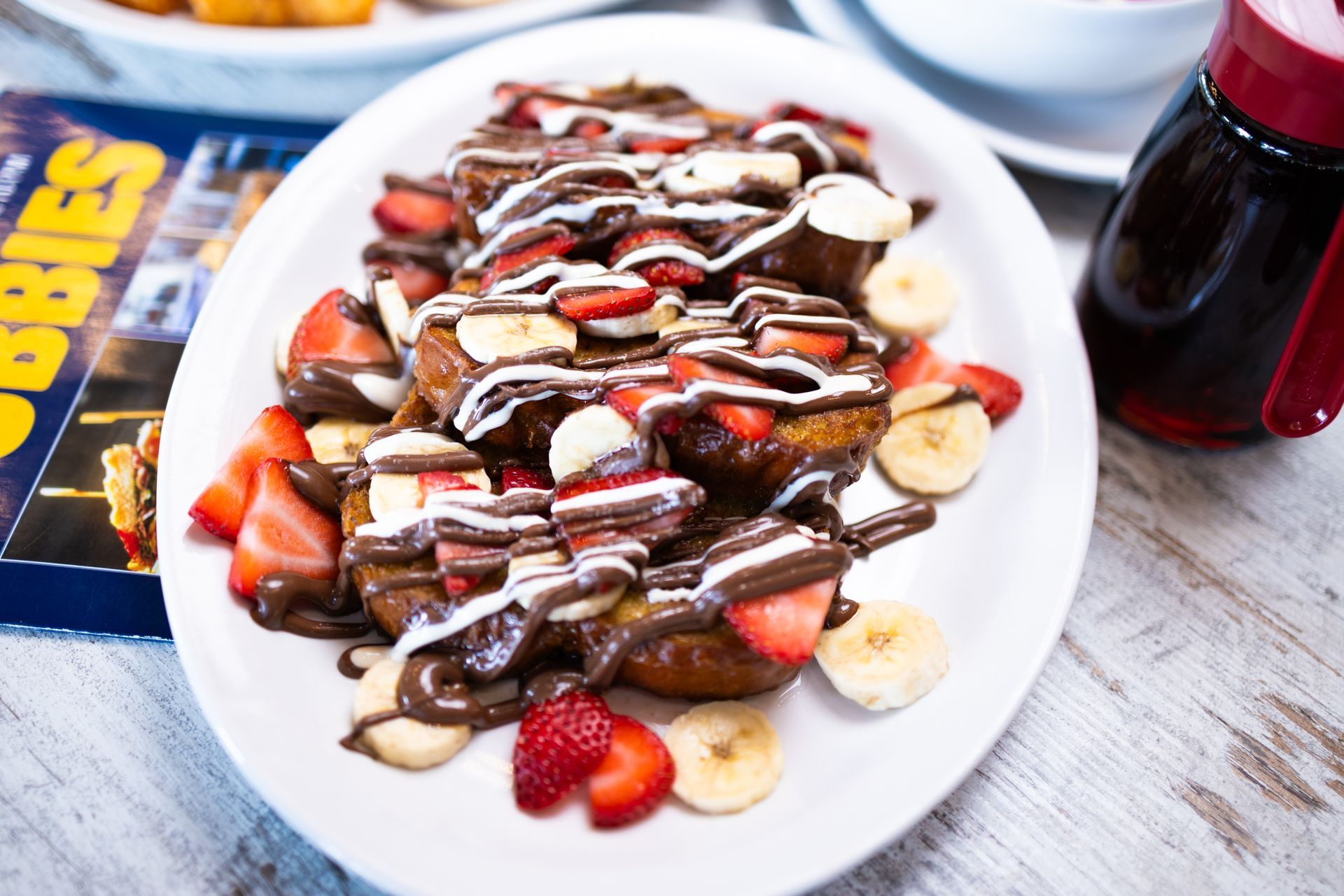 A plate of food with strawberries , bananas and chocolate on a table.