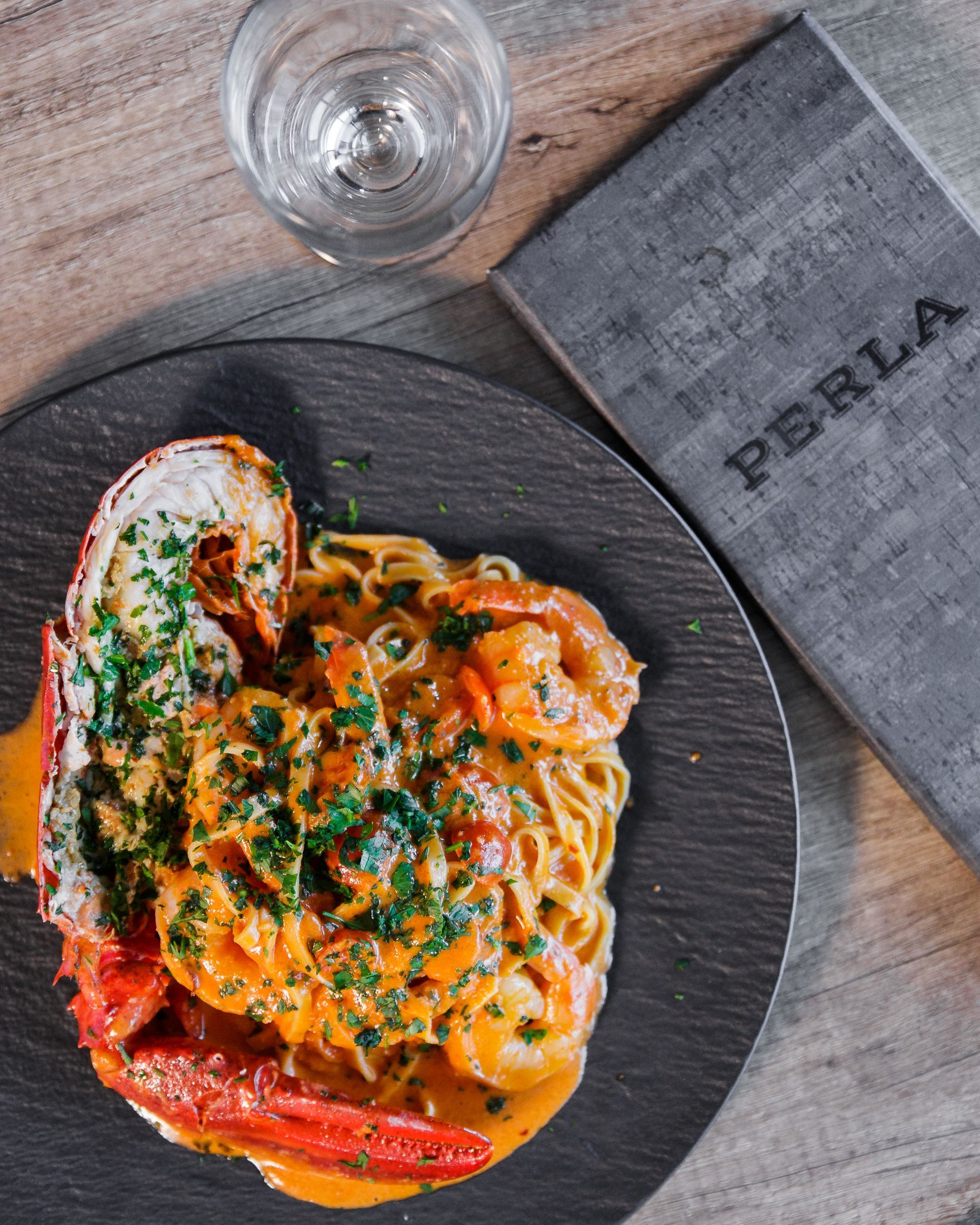 A plate of spaghetti with lobster and shrimp next to a menu for perla
