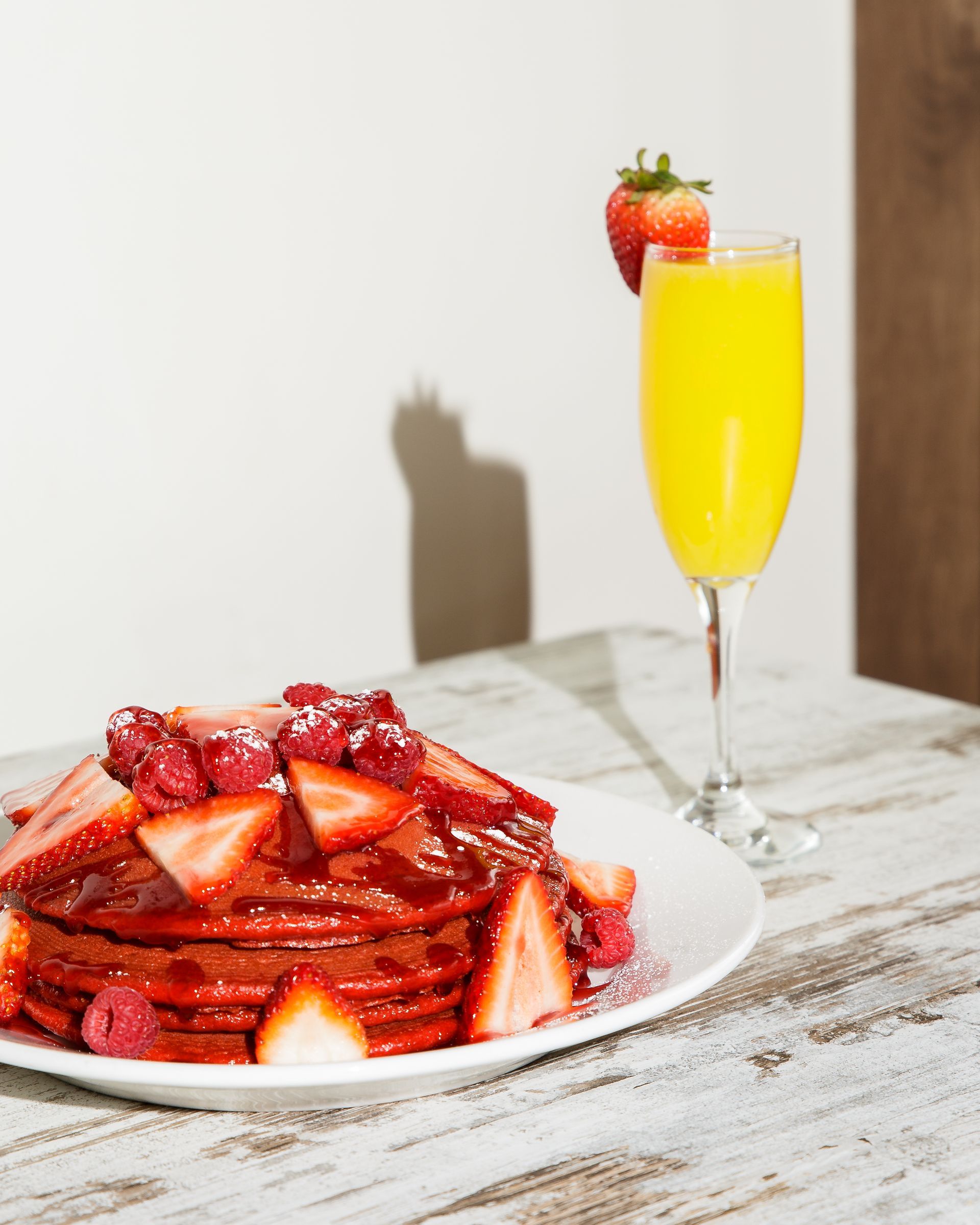 A plate of pancakes with strawberries and a glass of orange juice on a table.