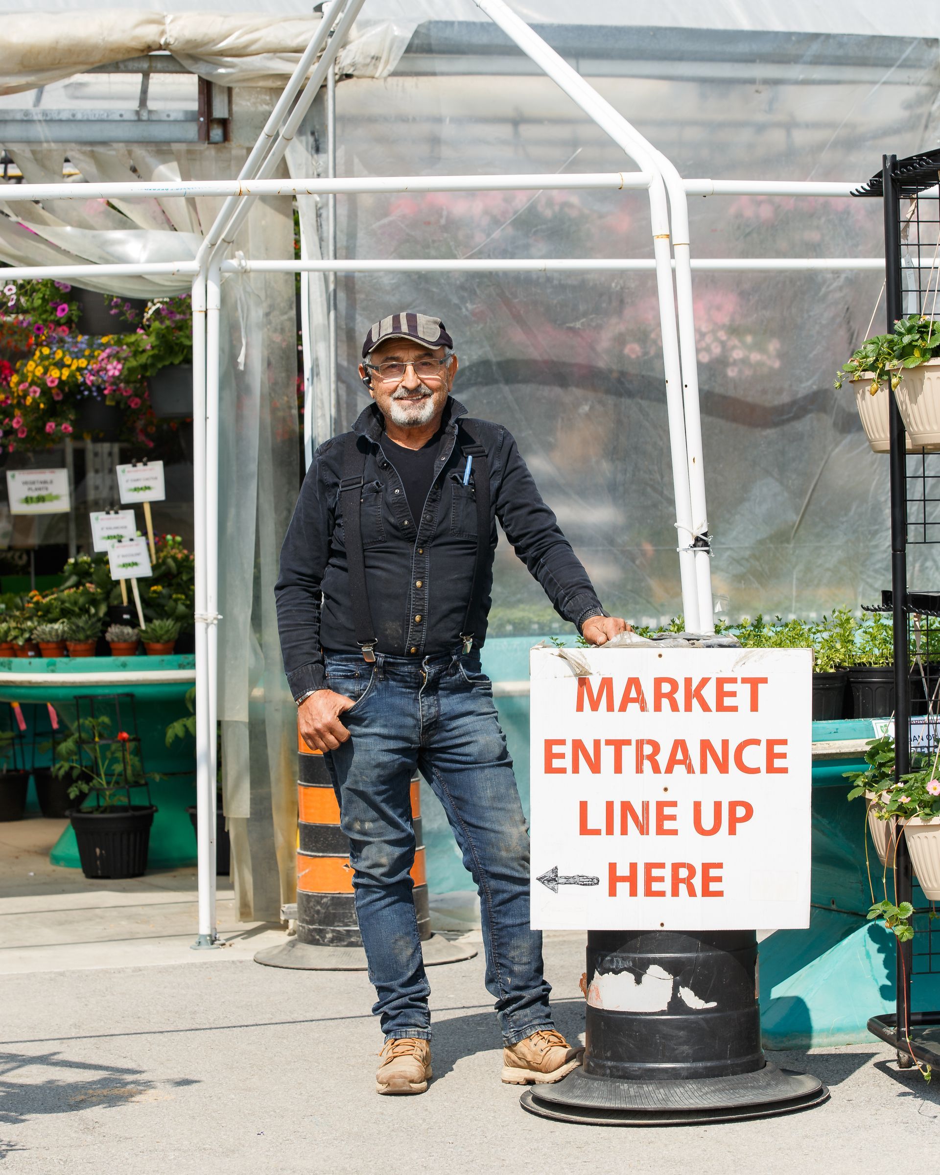 A man is standing in front of a greenhouse holding a sign that says market entrance line up here.