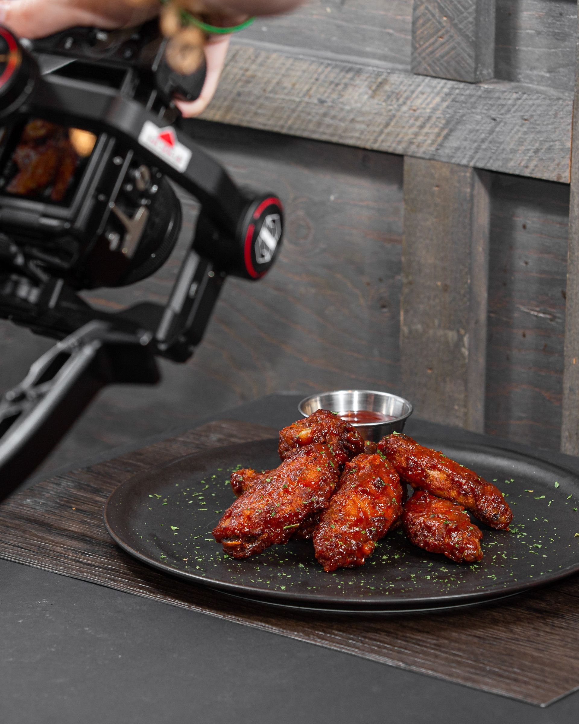 A person is taking a picture of chicken wings on a plate