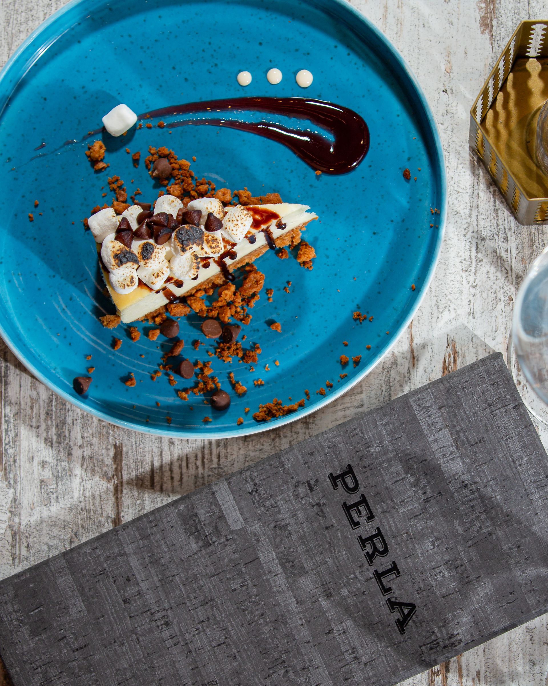 A blue plate with a piece of cake on it next to a napkin that says perla