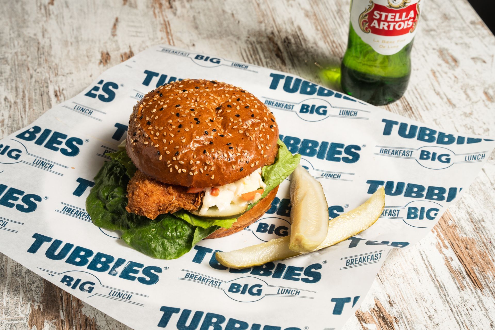 A hamburger and french fries are on a table next to a bottle of beer.