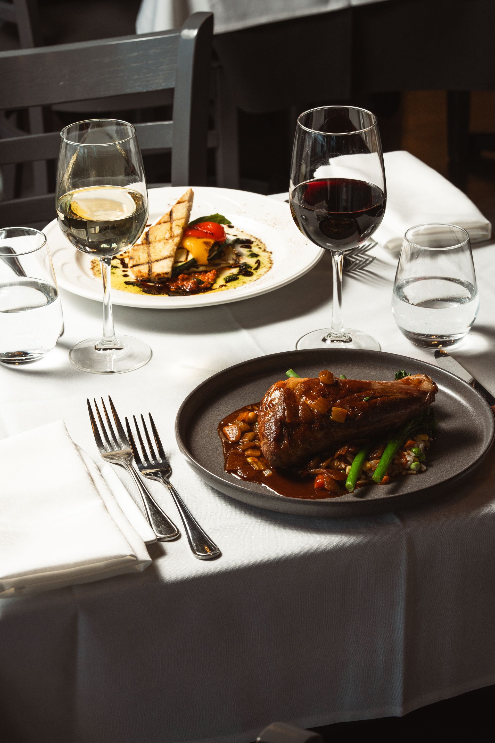 Two plates of food and two glasses of wine are on a table.