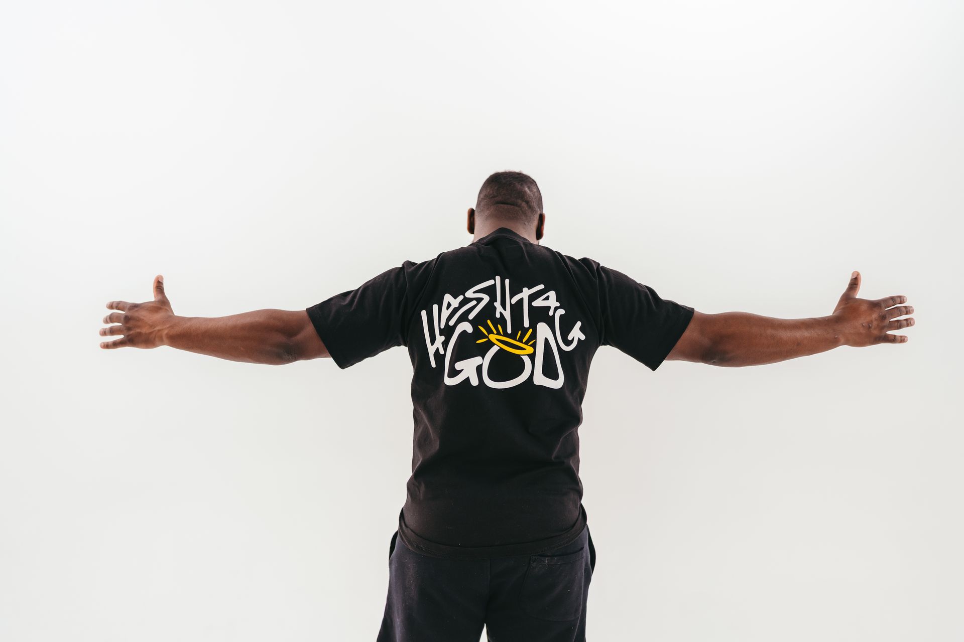 A man in a black t-shirt is standing with his arms outstretched.