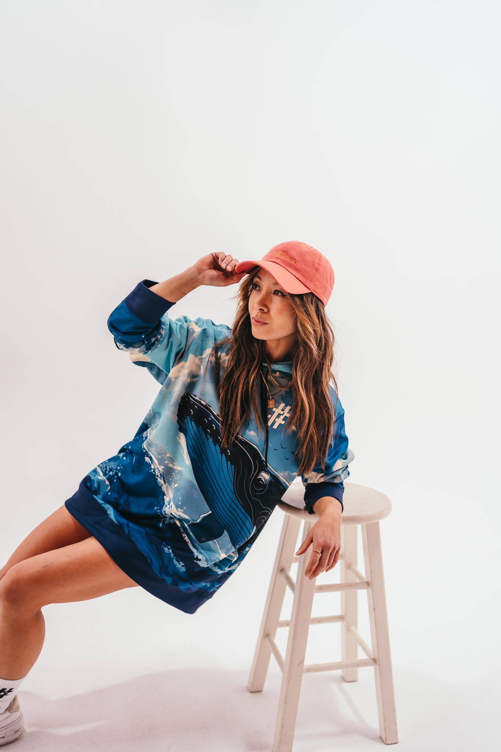A woman is sitting on a stool wearing a hat and a sweater.