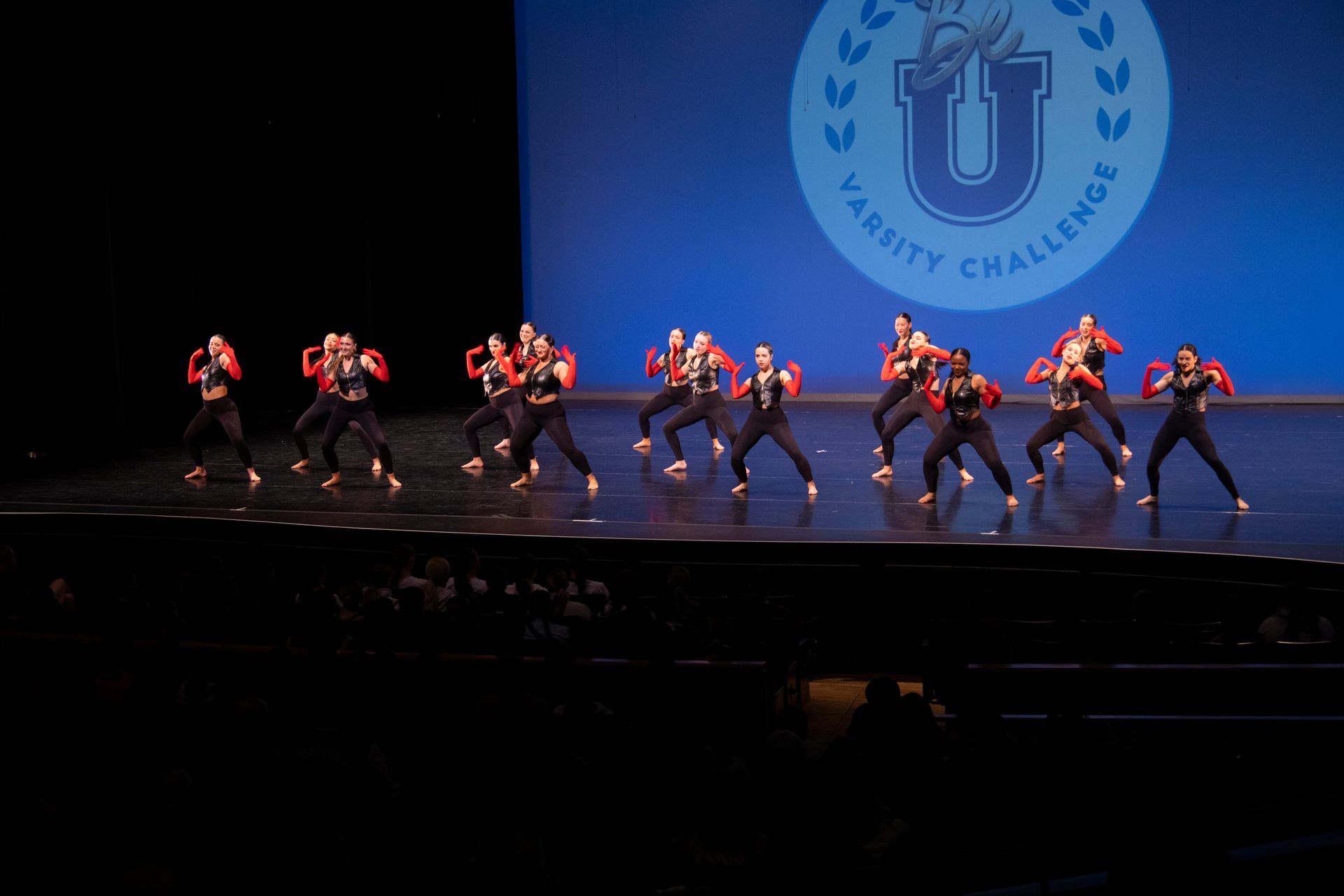 A group of people are dancing on a stage in front of a sign that says varsity challenge.