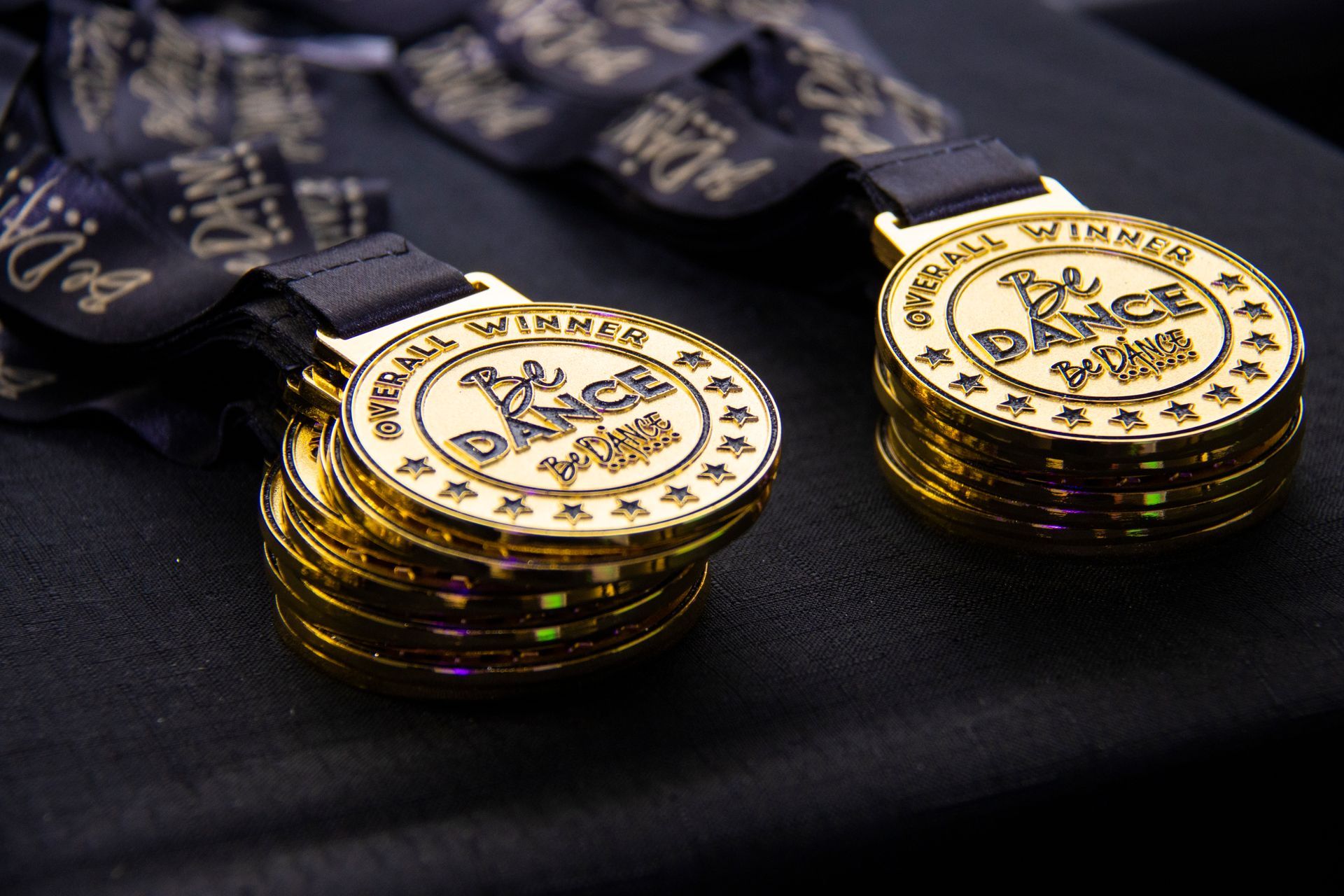 Two gold medals are stacked on top of each other on a black surface.