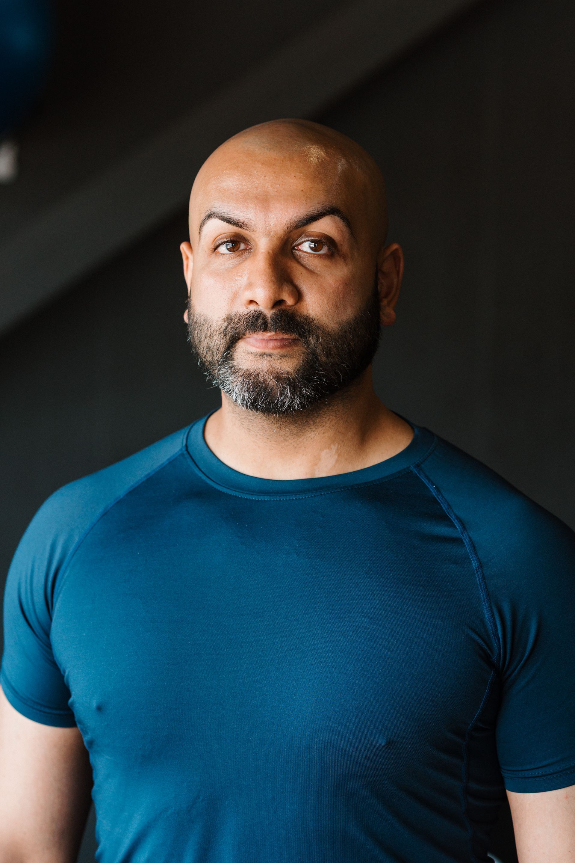 A bald man with a beard is wearing a blue t-shirt and looking at the camera.