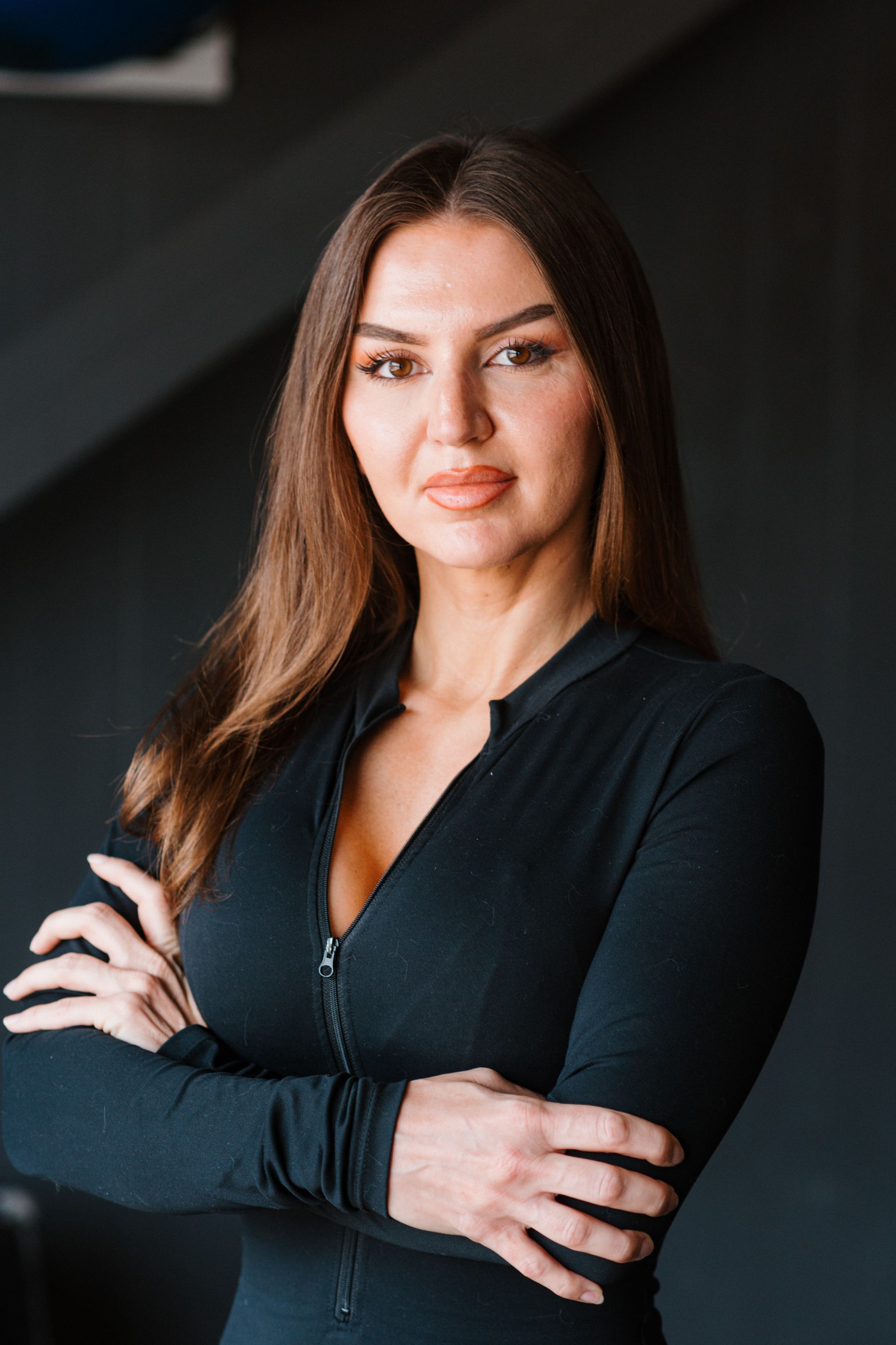 A woman in a black dress is standing with her arms crossed.