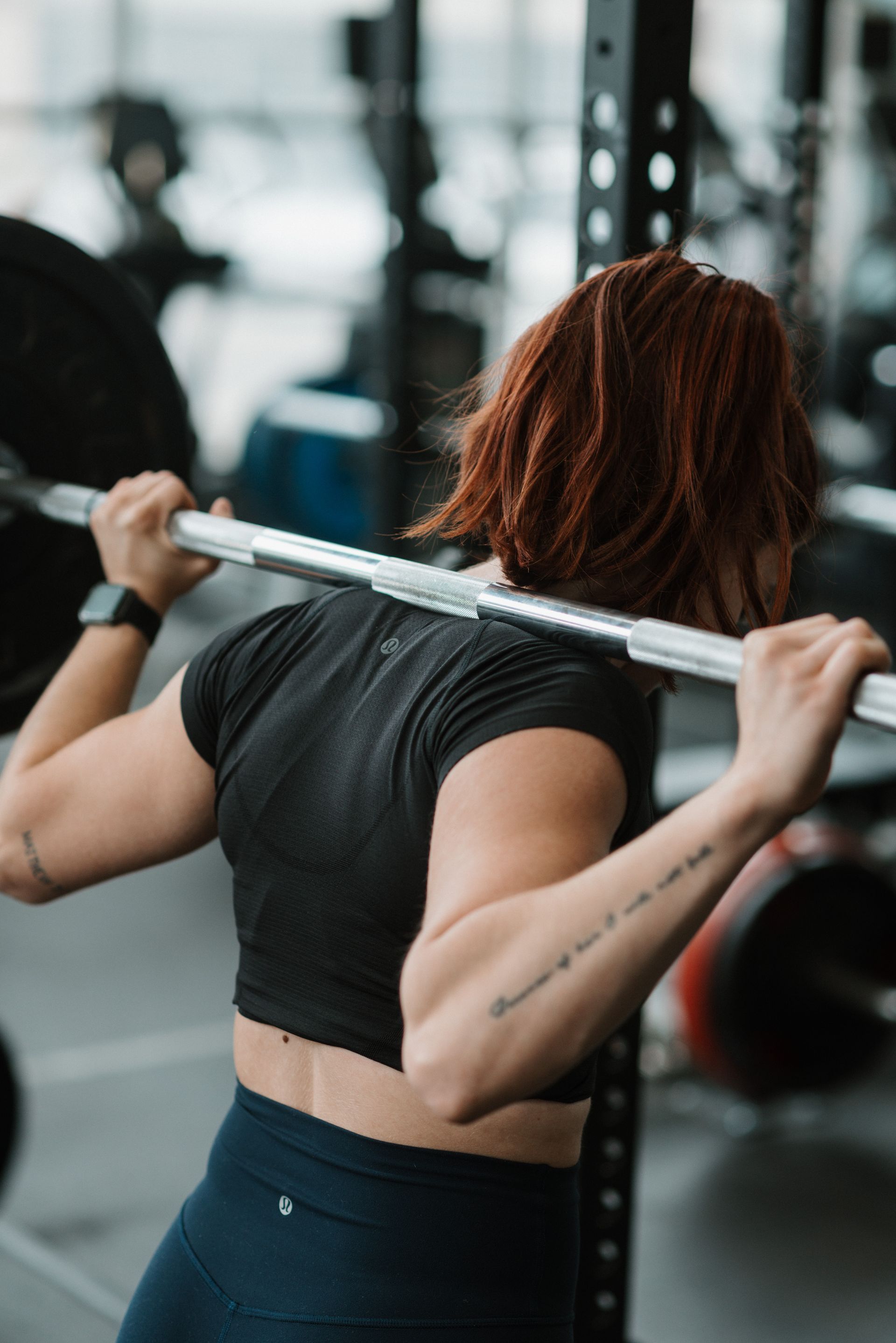 A woman is squatting with a barbell over her head in a gym.