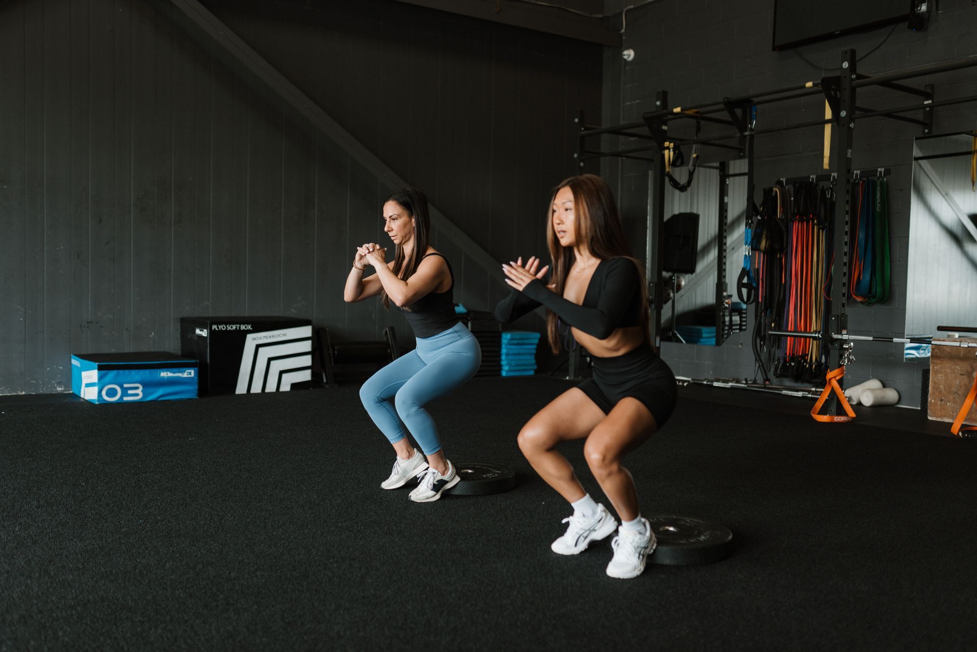Two women are doing squats in a gym.