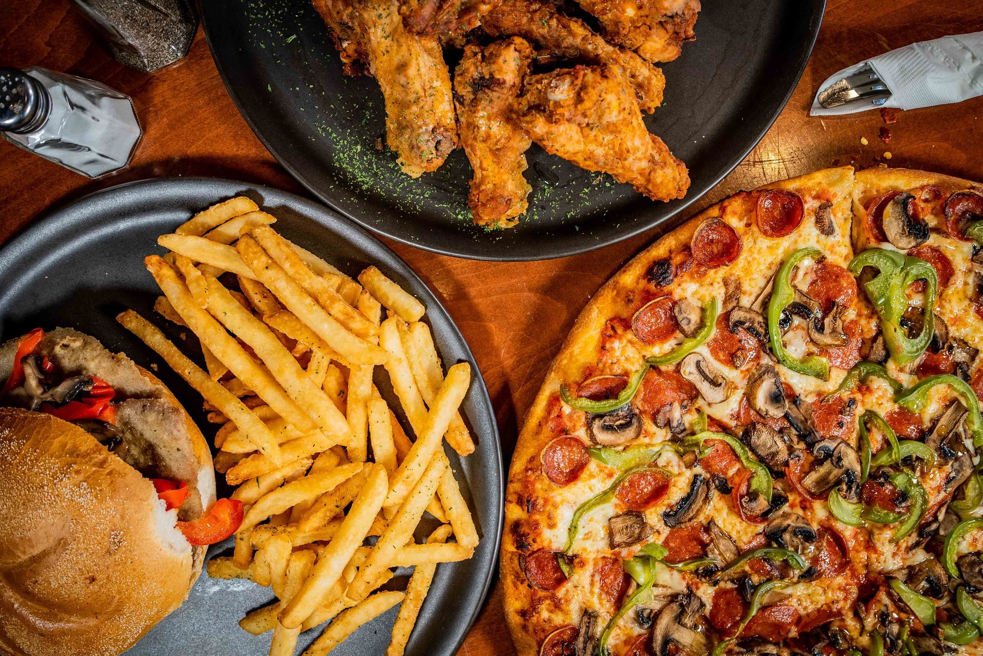 A pizza , french fries , chicken wings and a hamburger are on a table.