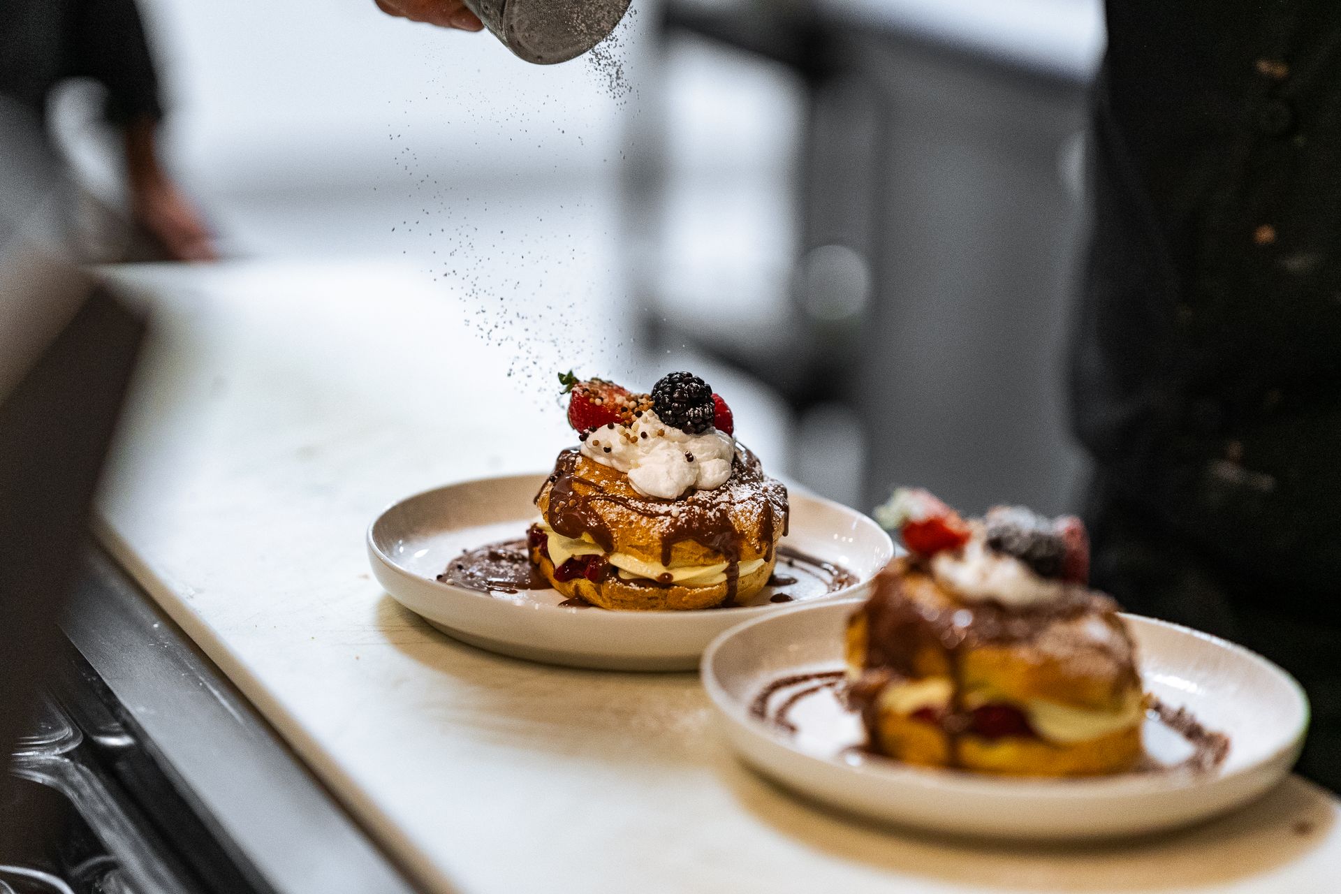 A person is sprinkling sugar on a dessert on a plate.