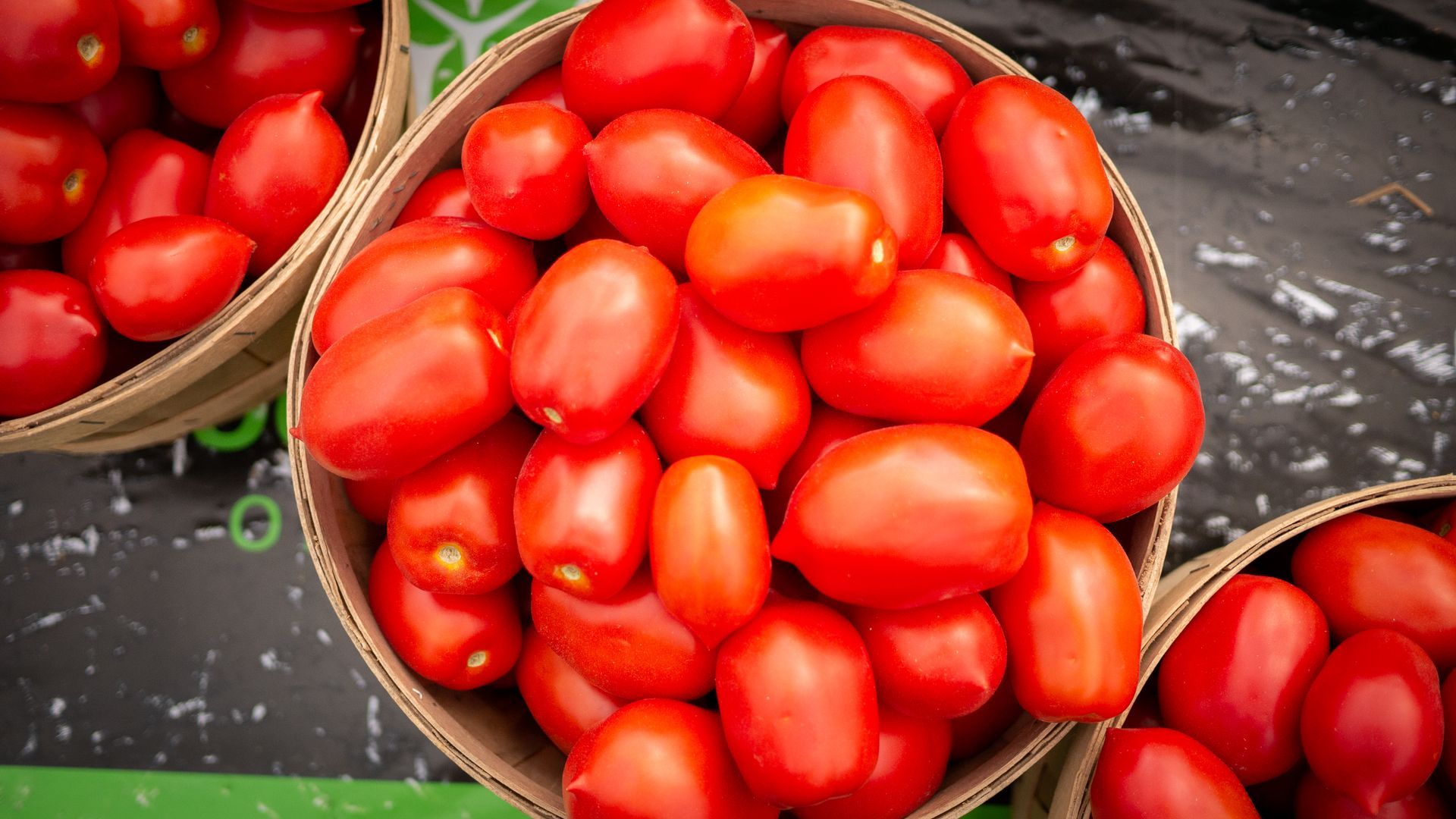 A basket filled with red tomatoes is sitting on a table.