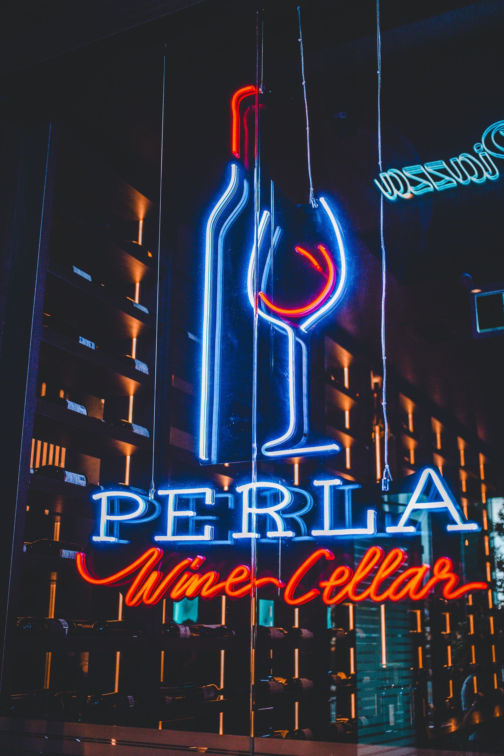 A neon sign for perla wine cellars is lit up at night