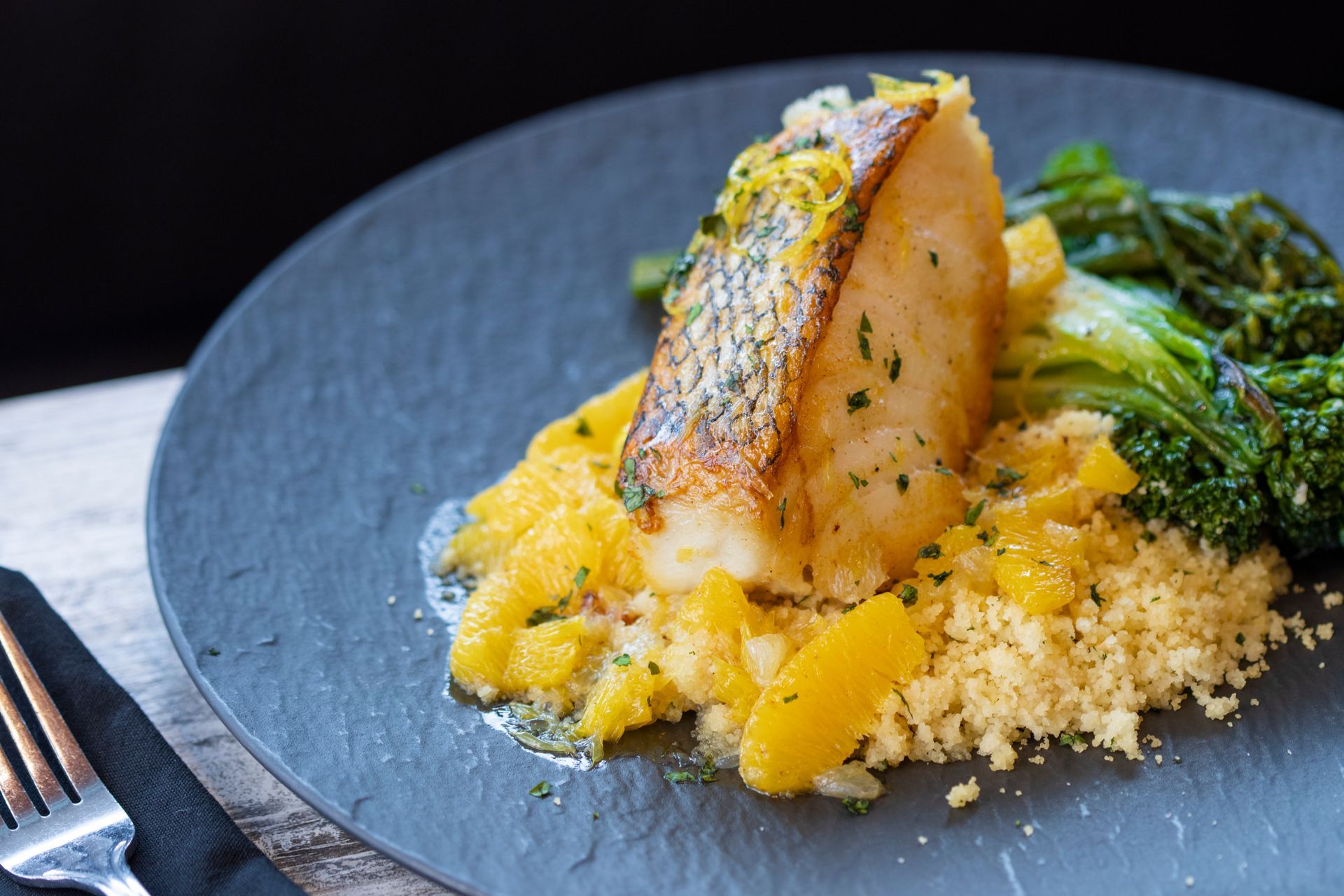 A black plate topped with a piece of fish and vegetables.