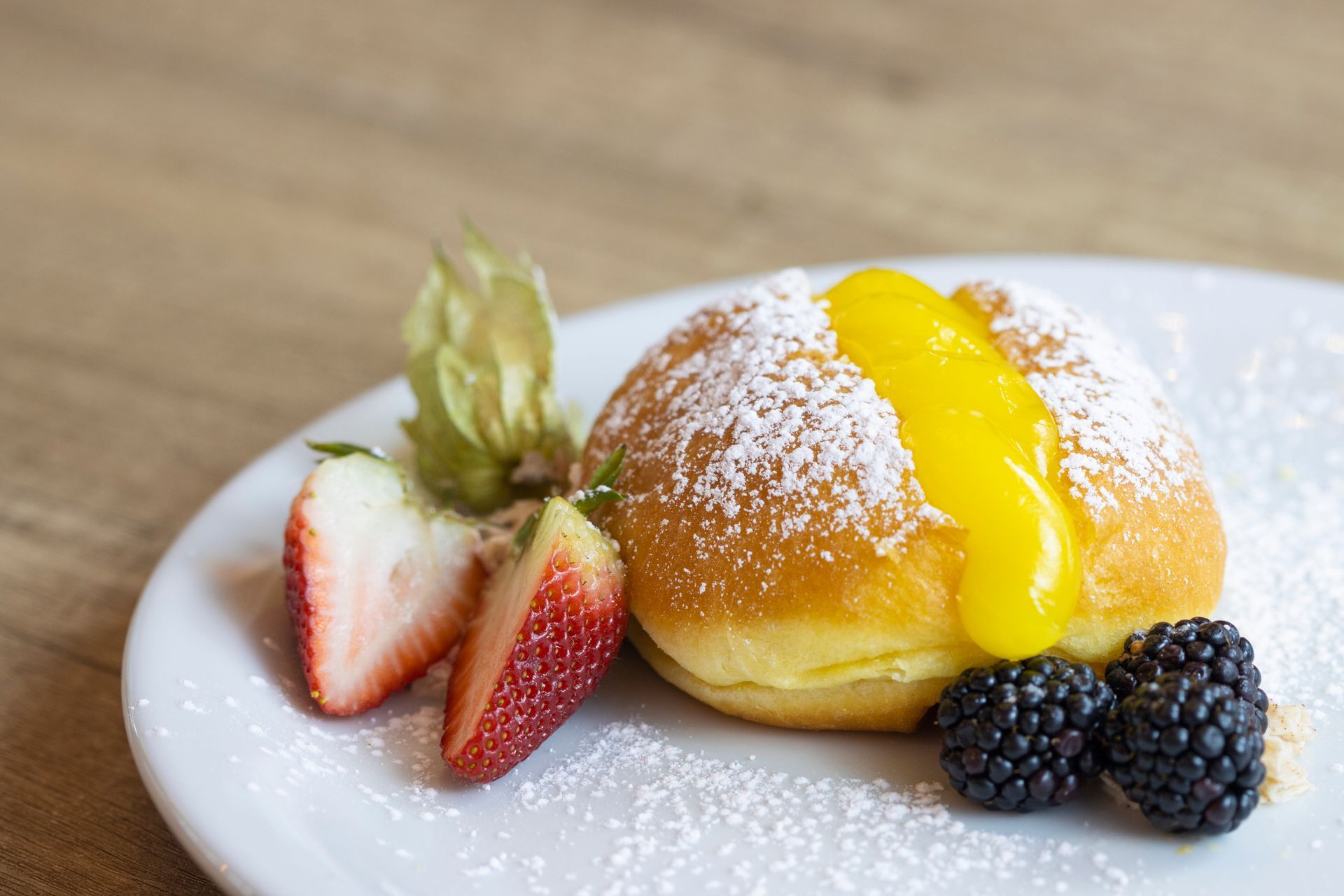 A white plate topped with a donut , berries and powdered sugar.