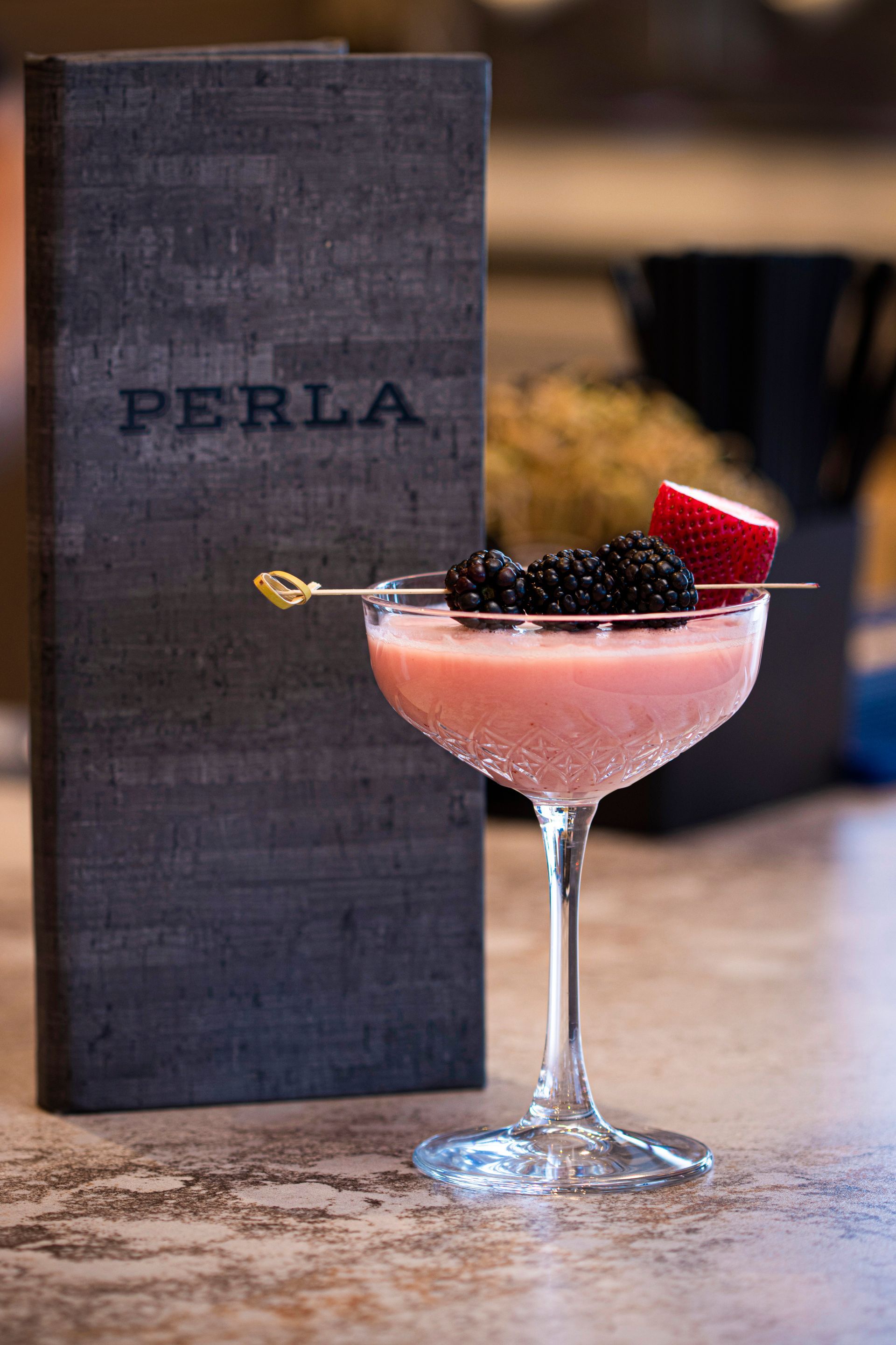 A martini glass filled with pink liquid and berries next to a menu.