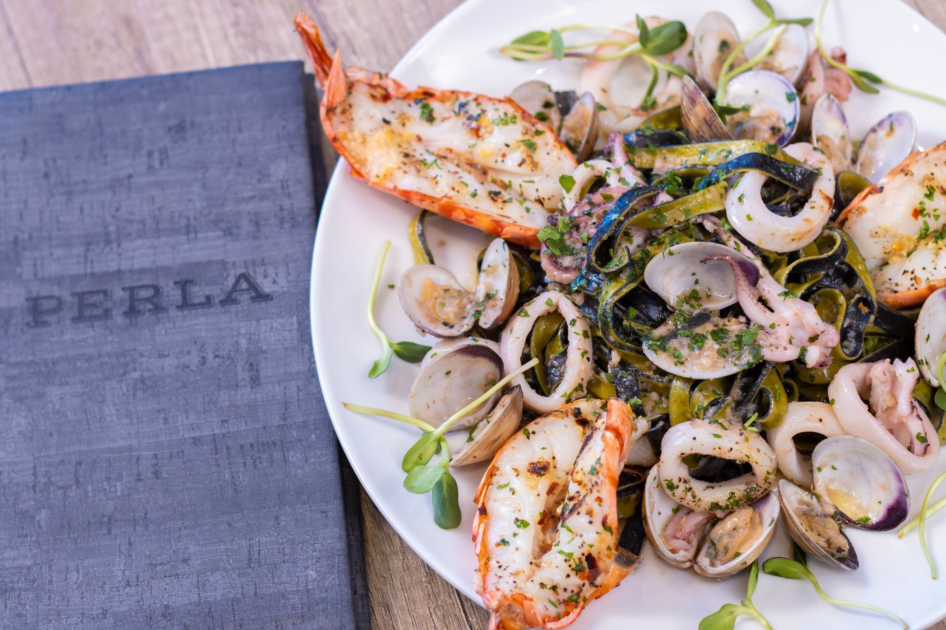 A plate of seafood sits next to a napkin that says perla