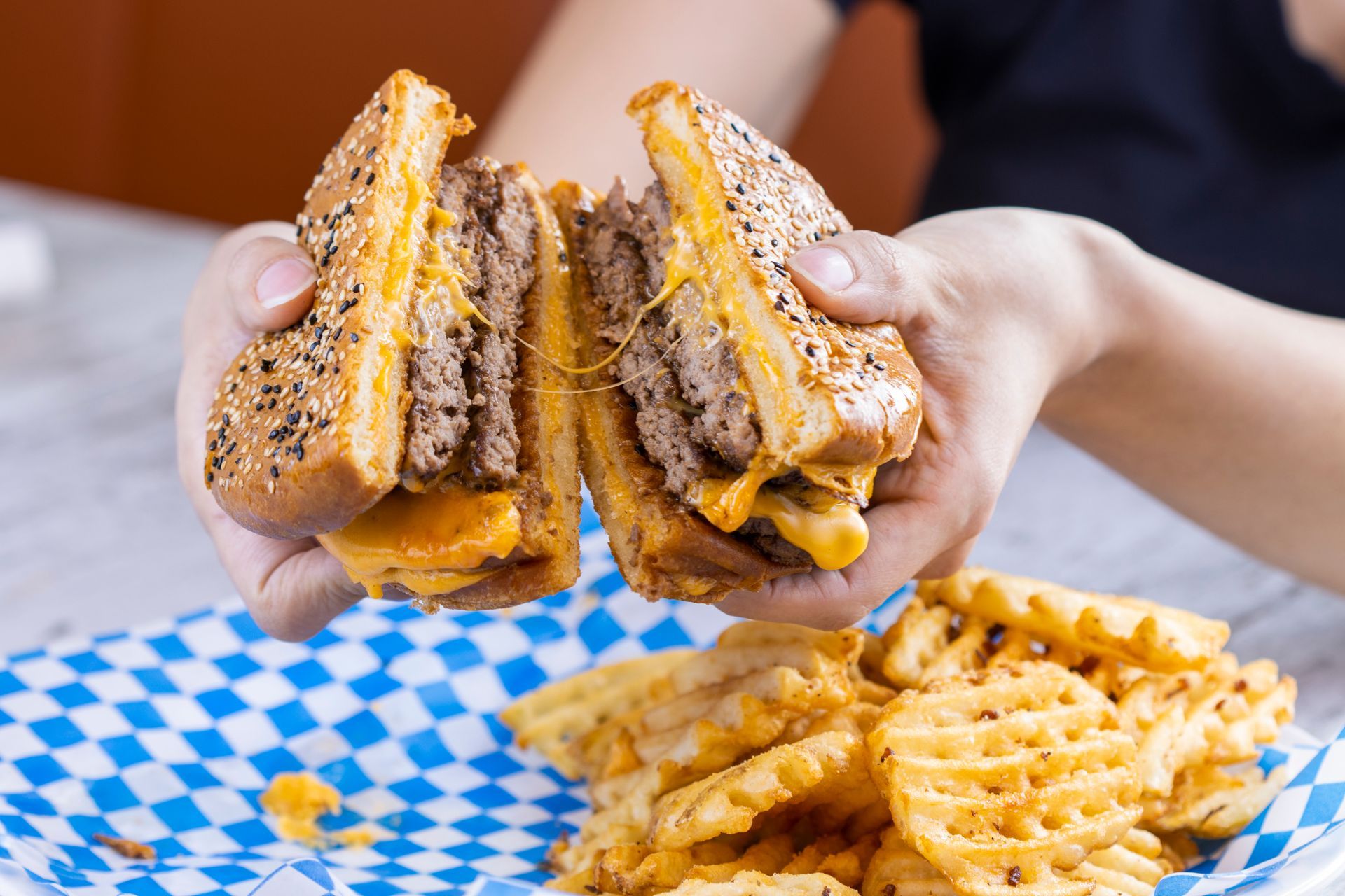 A person is holding a hamburger and french fries in their hands.