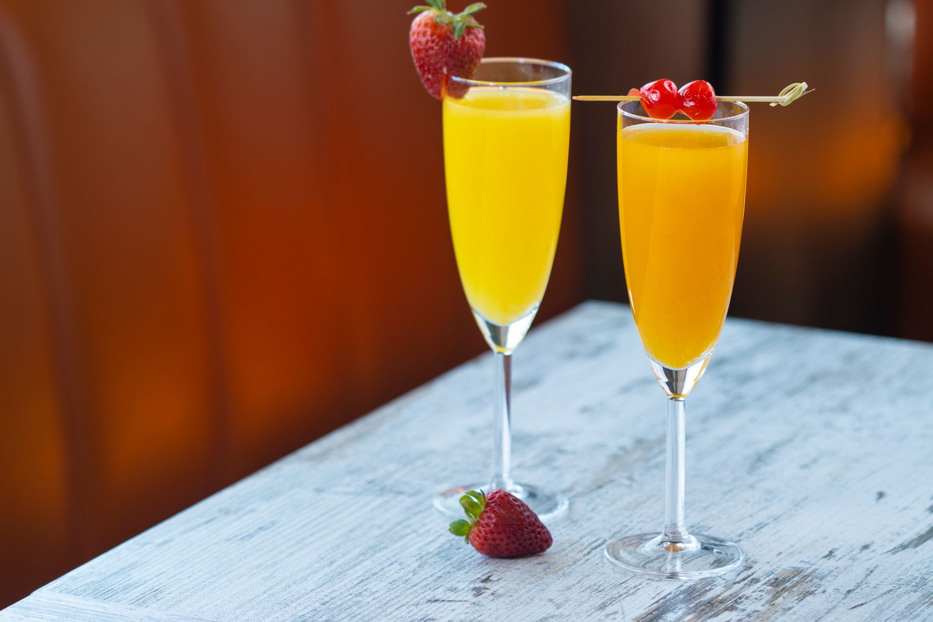 Two glasses of orange juice with strawberries and cherries on a table.
