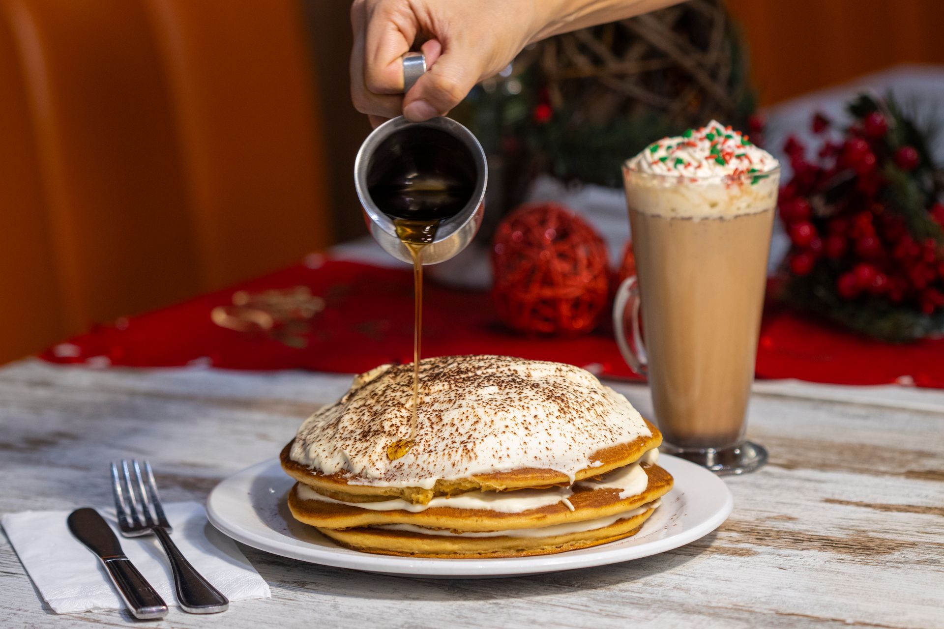 A person is pouring syrup on a stack of pancakes.