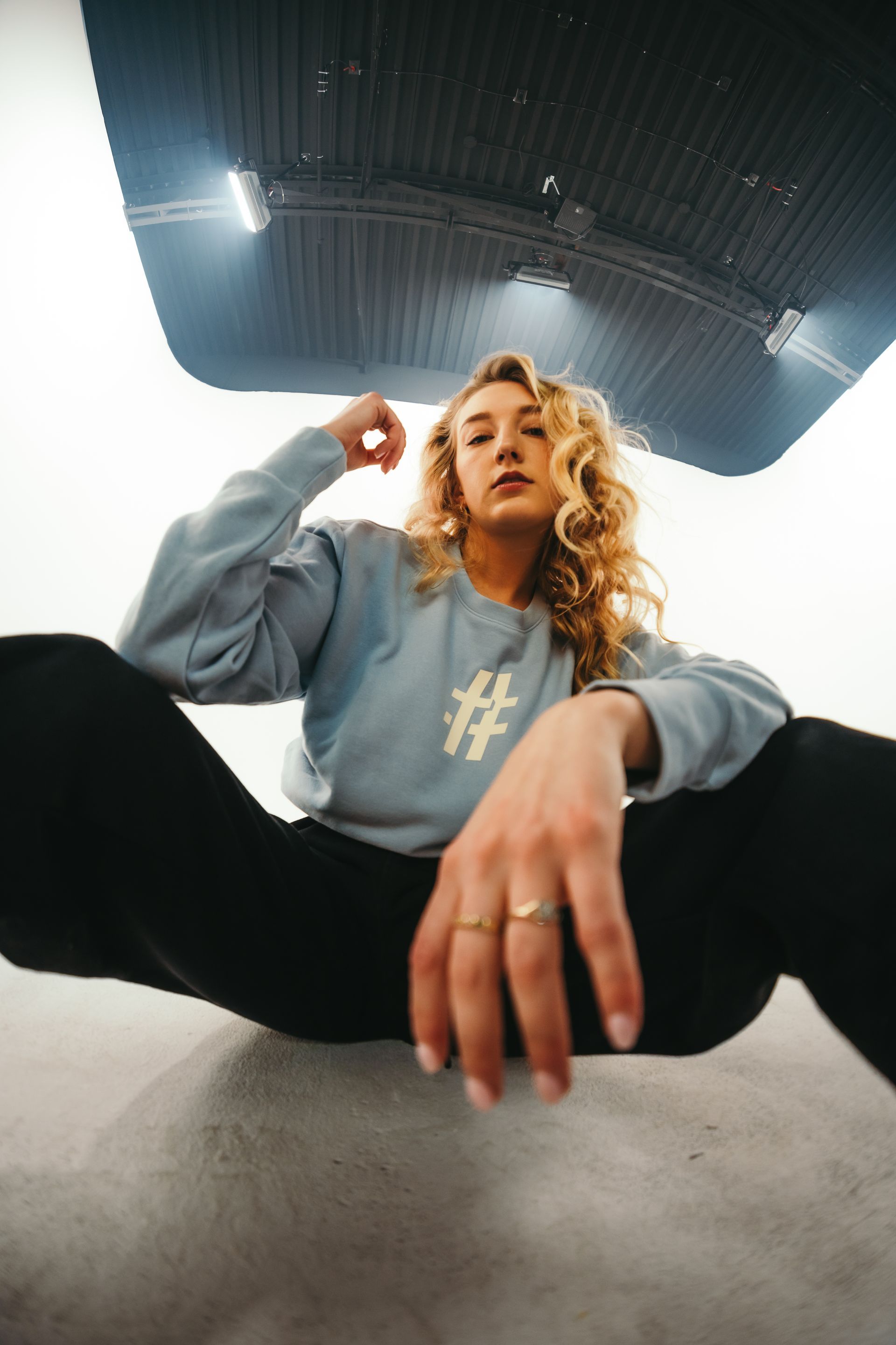 A woman is sitting on the floor wearing a blue sweater and black pants.