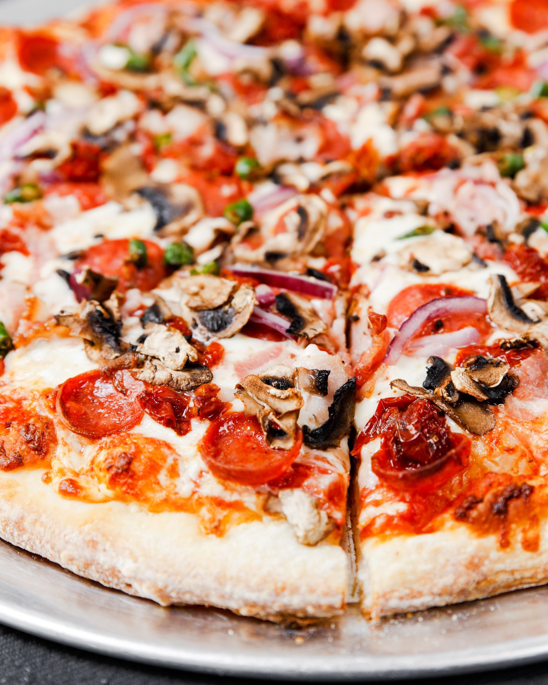 A pizza with pepperoni , mushrooms , onions and cheese is on a pan.