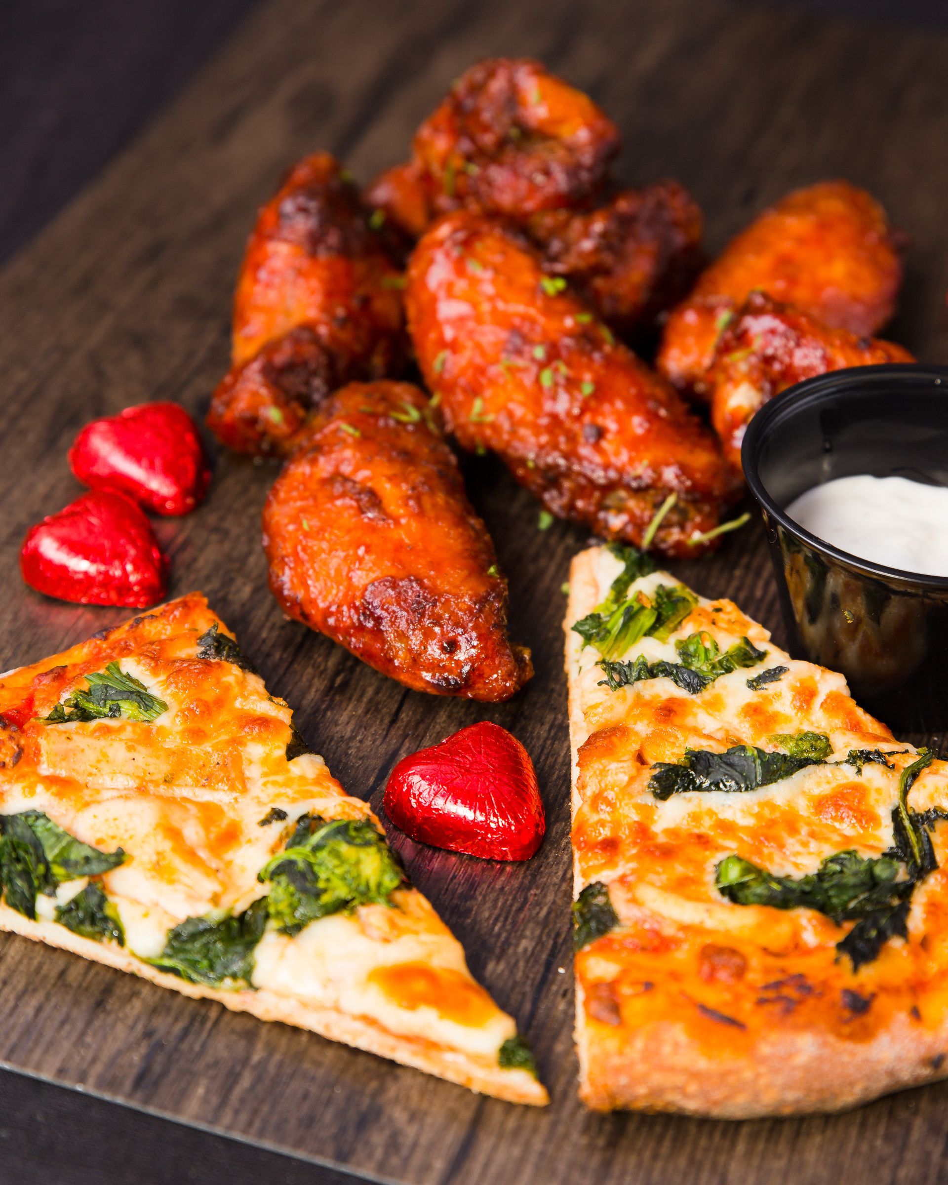 A pizza and chicken wings are on a wooden cutting board.