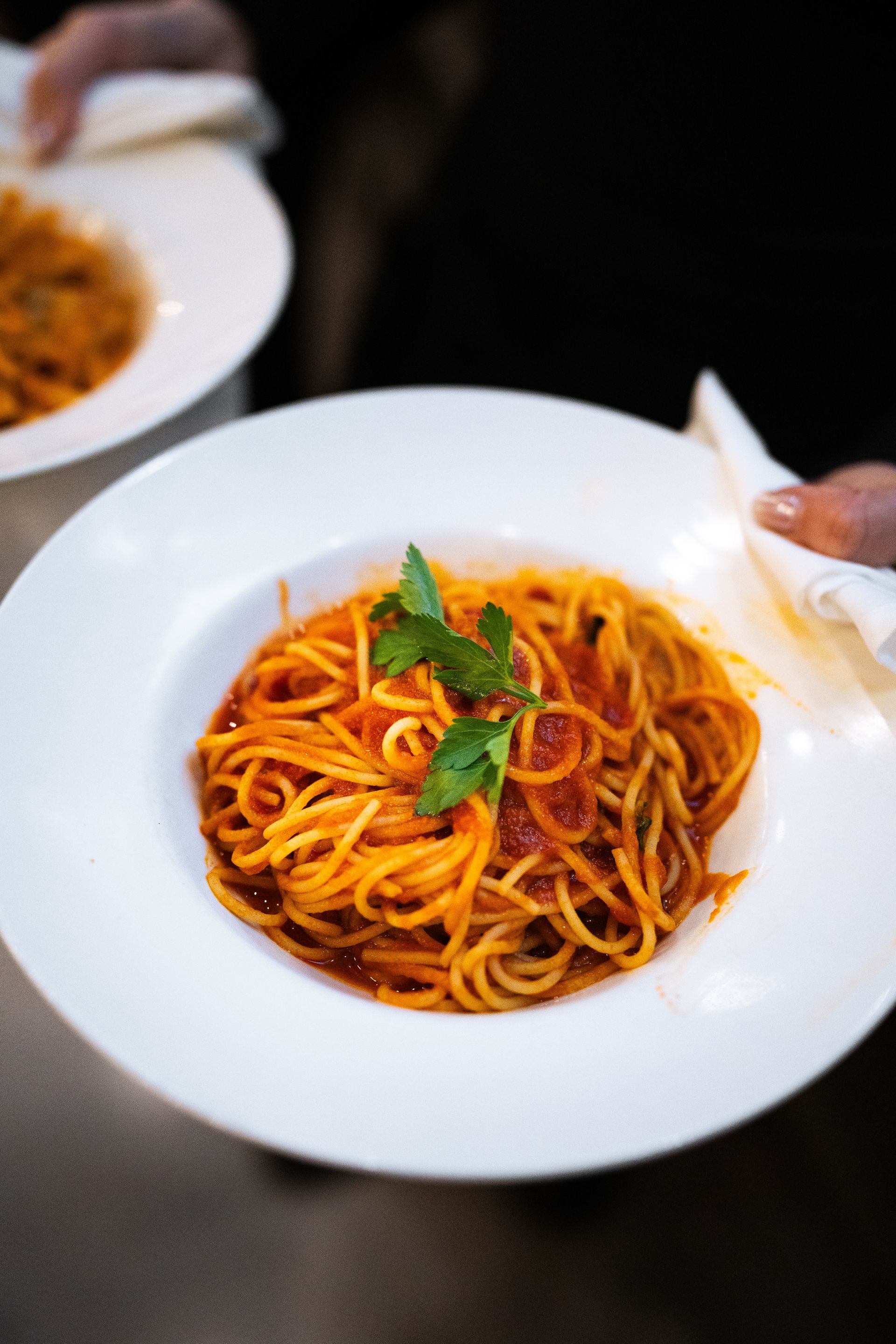 A person is holding a plate of spaghetti with tomato sauce.