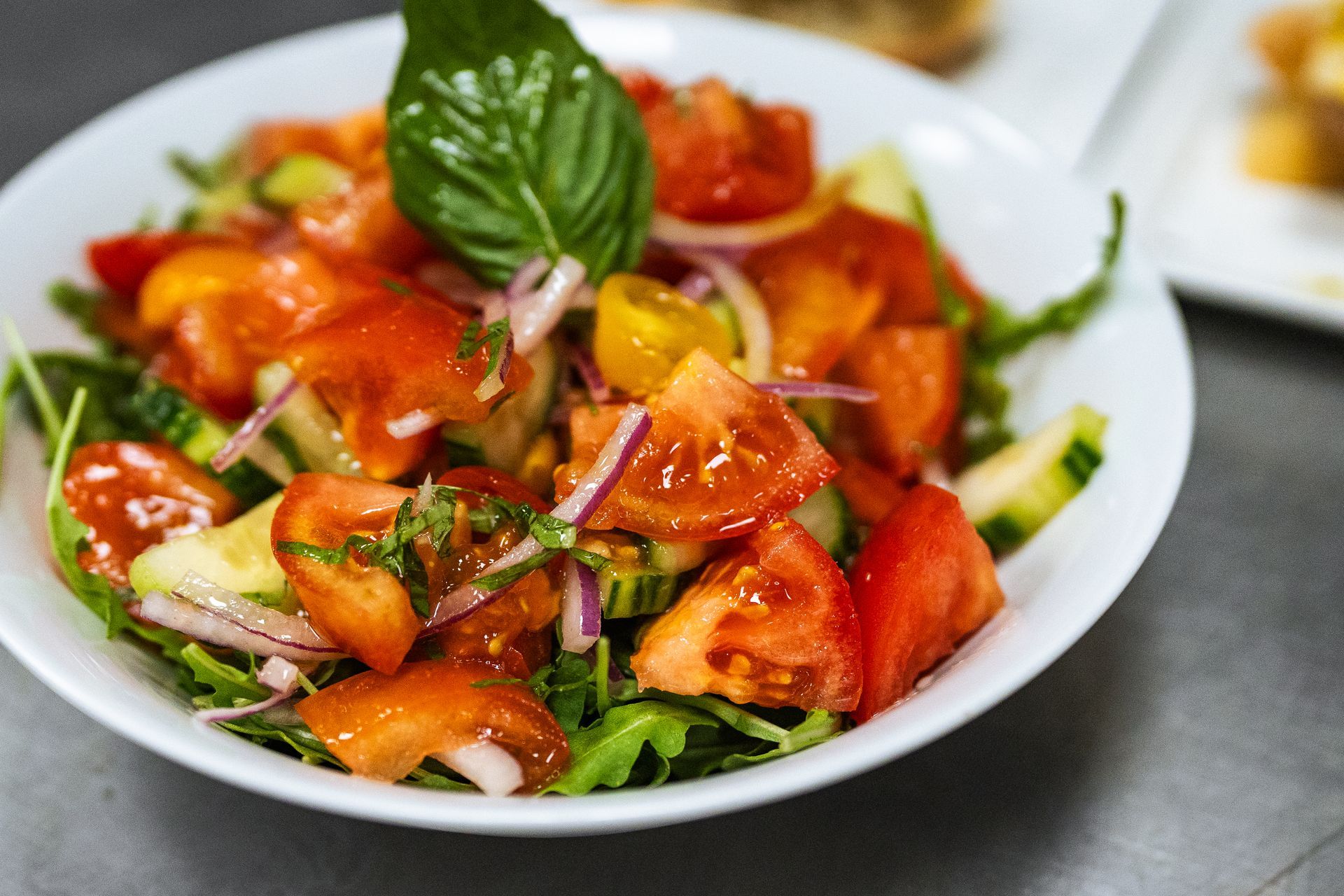 A salad with tomatoes , cucumbers , onions and basil in a white bowl.