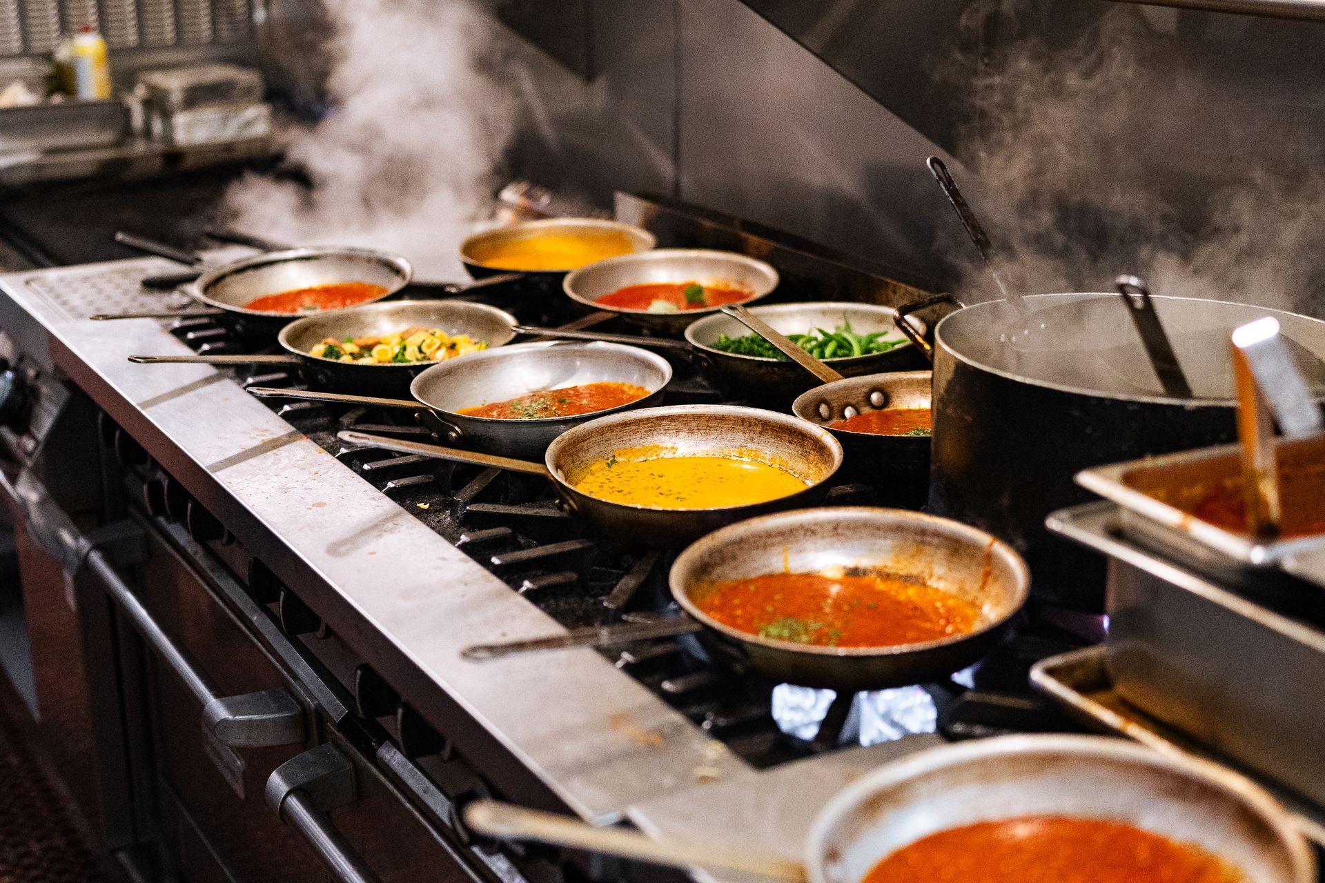 A row of pots and pans cooking on a stove in a kitchen.