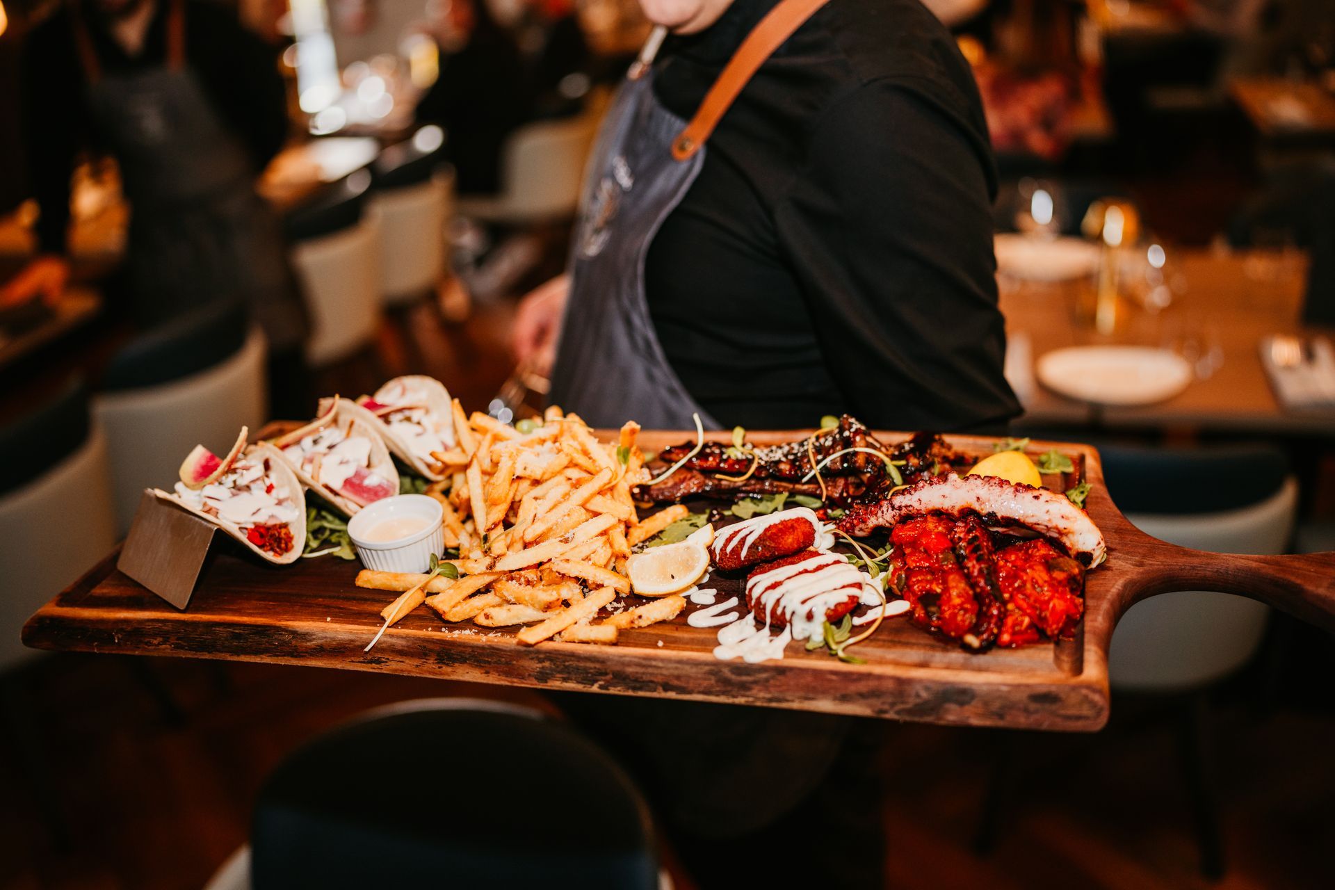 A waiter is carrying a wooden tray of food in a restaurant.