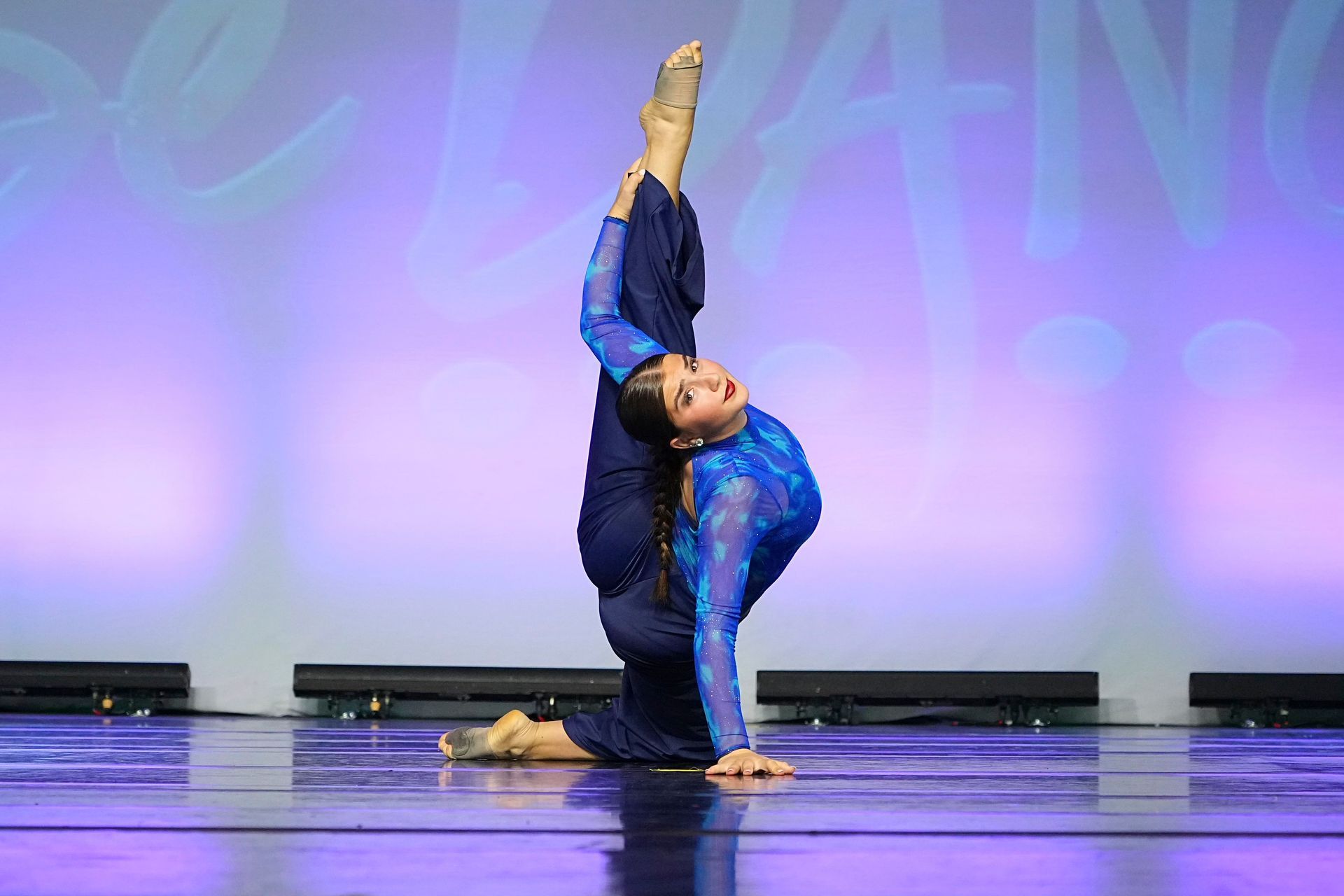 A woman in a blue dress is doing a split on a stage.