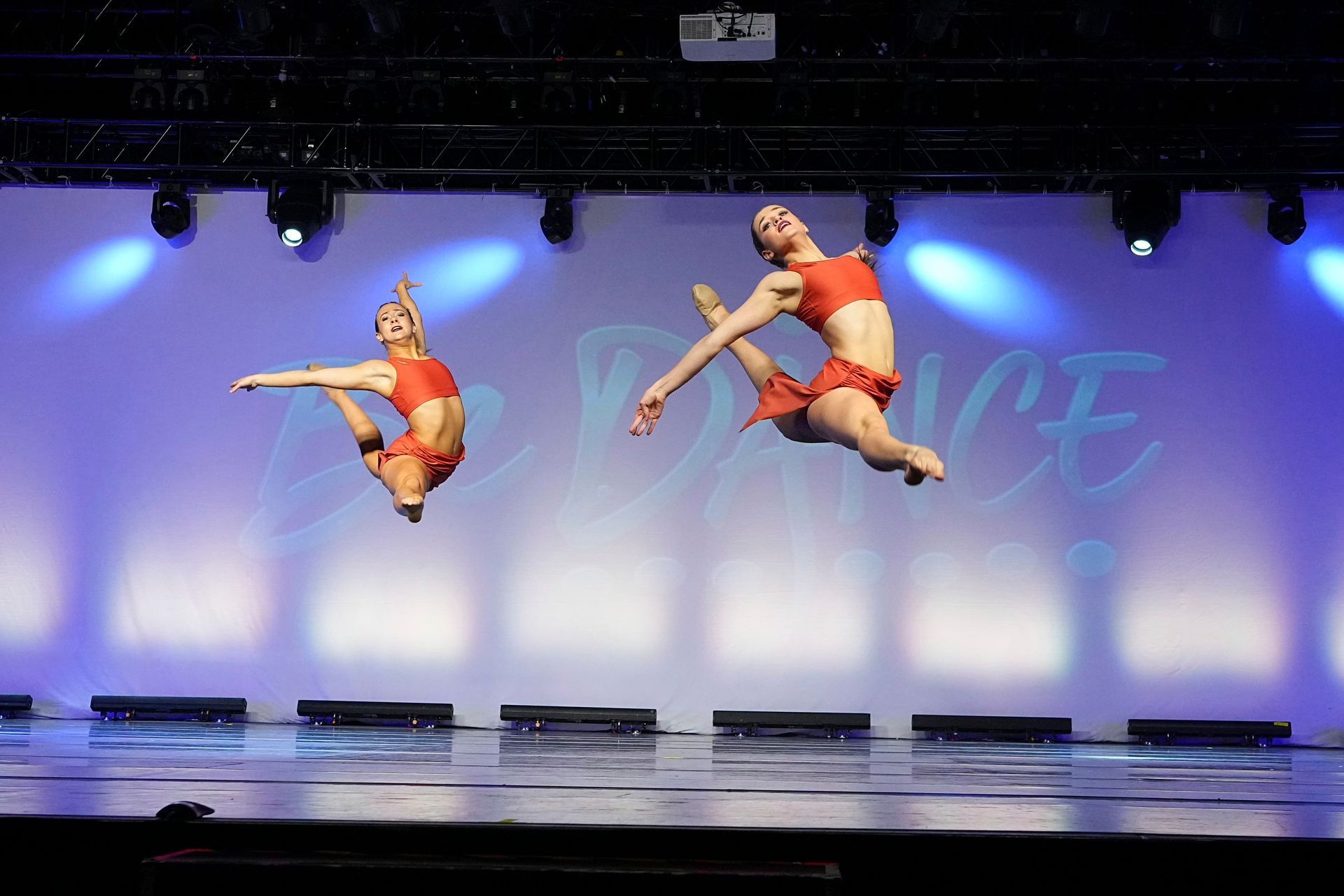 Two dancers are jumping in the air on a stage with the word dance in the background