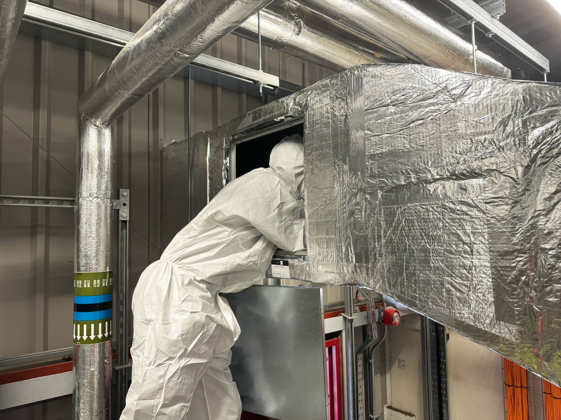 A man in a white suit is working on a machine in a room.