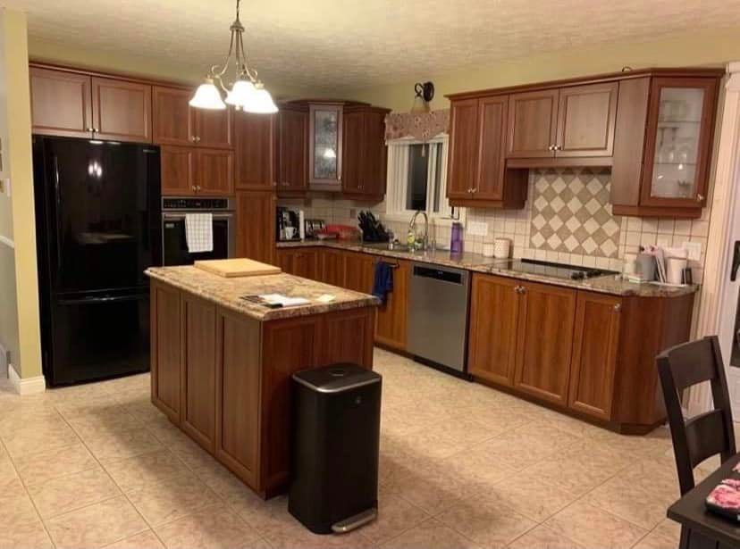 Une cuisine avec des armoires en bois, des électroménagers en acier inoxydable, un grand îlot et un réfrigérateur noir.