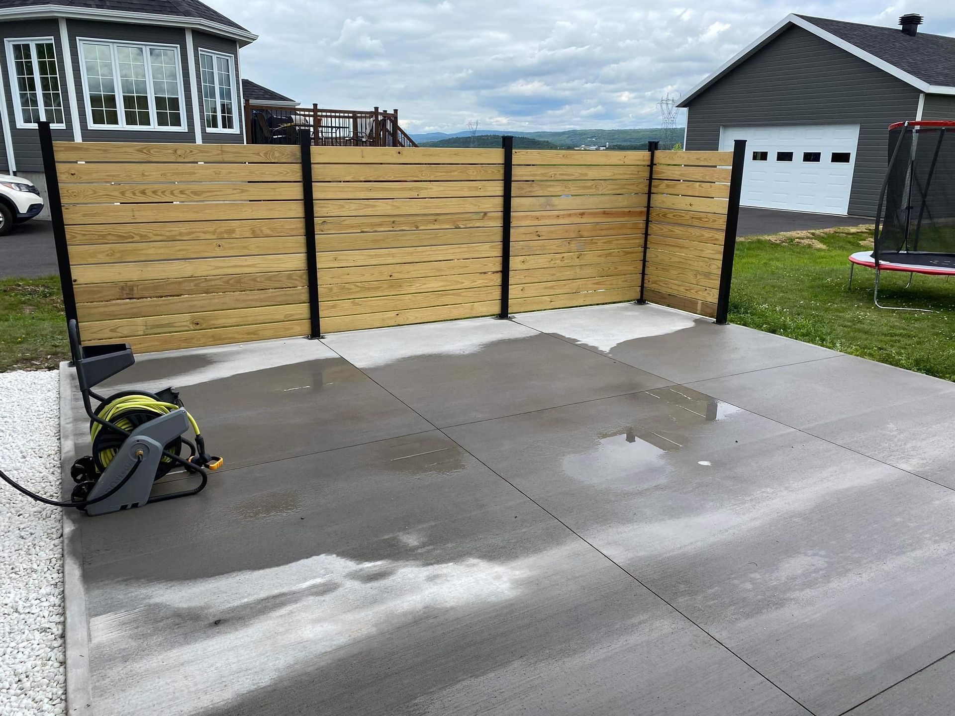 Un patio en béton avec une clôture en bois et un trampoline en arrière-plan.