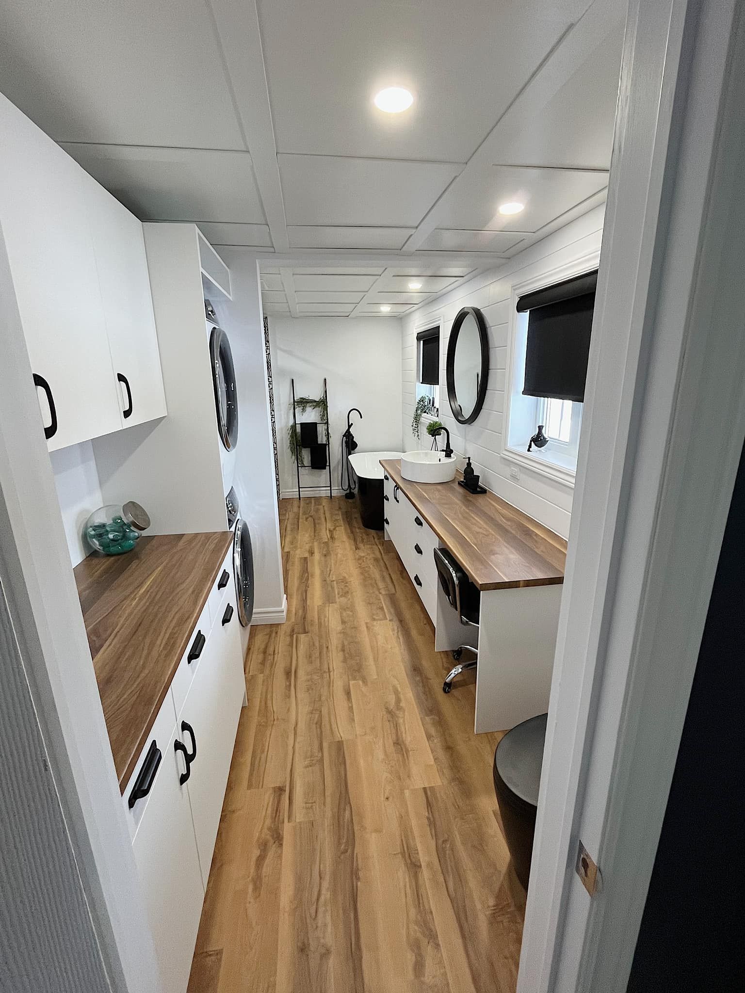 Un long couloir avec parquet et armoires blanches menant à une salle de bain.