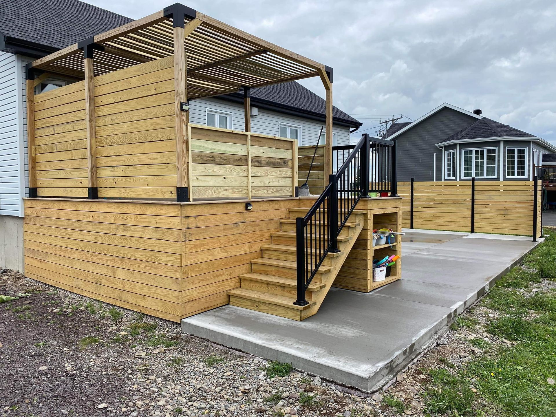 Une terrasse en bois avec des escaliers et une pergola devant une maison.